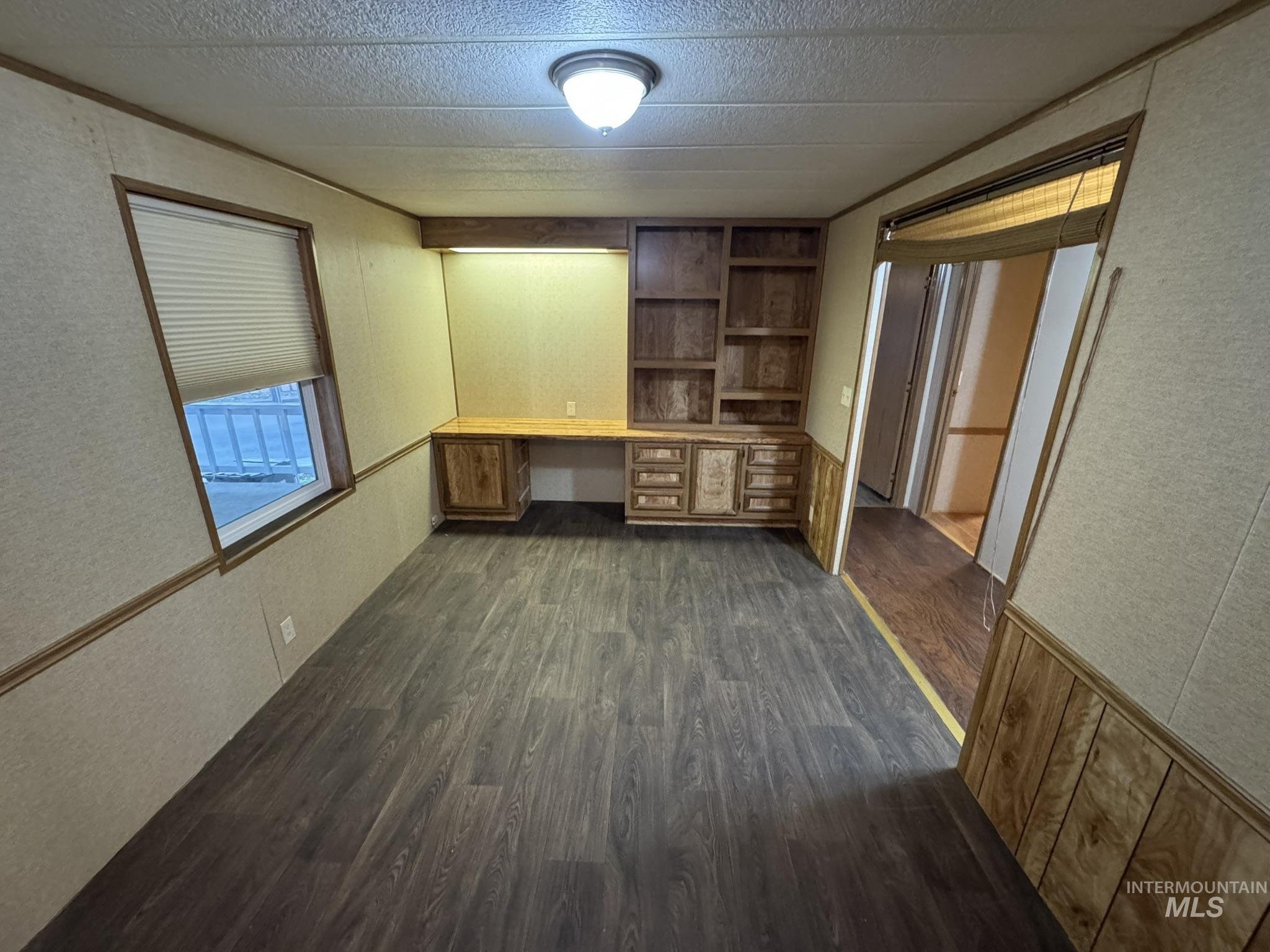 Unfurnished office with built in desk, dark wood-style flooring, and a textured wall