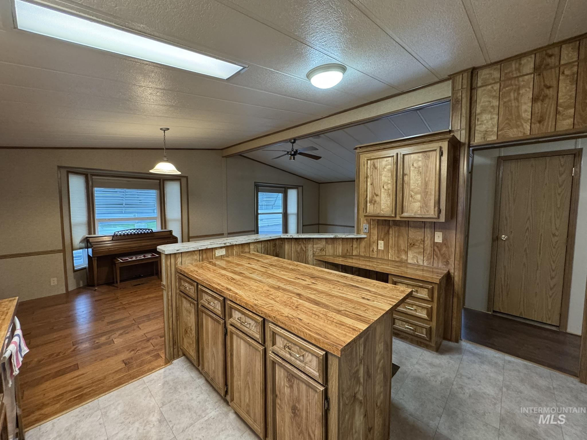 Kitchen featuring brown cabinets, ceiling fan, a peninsula, wood counters, and pendant lighting