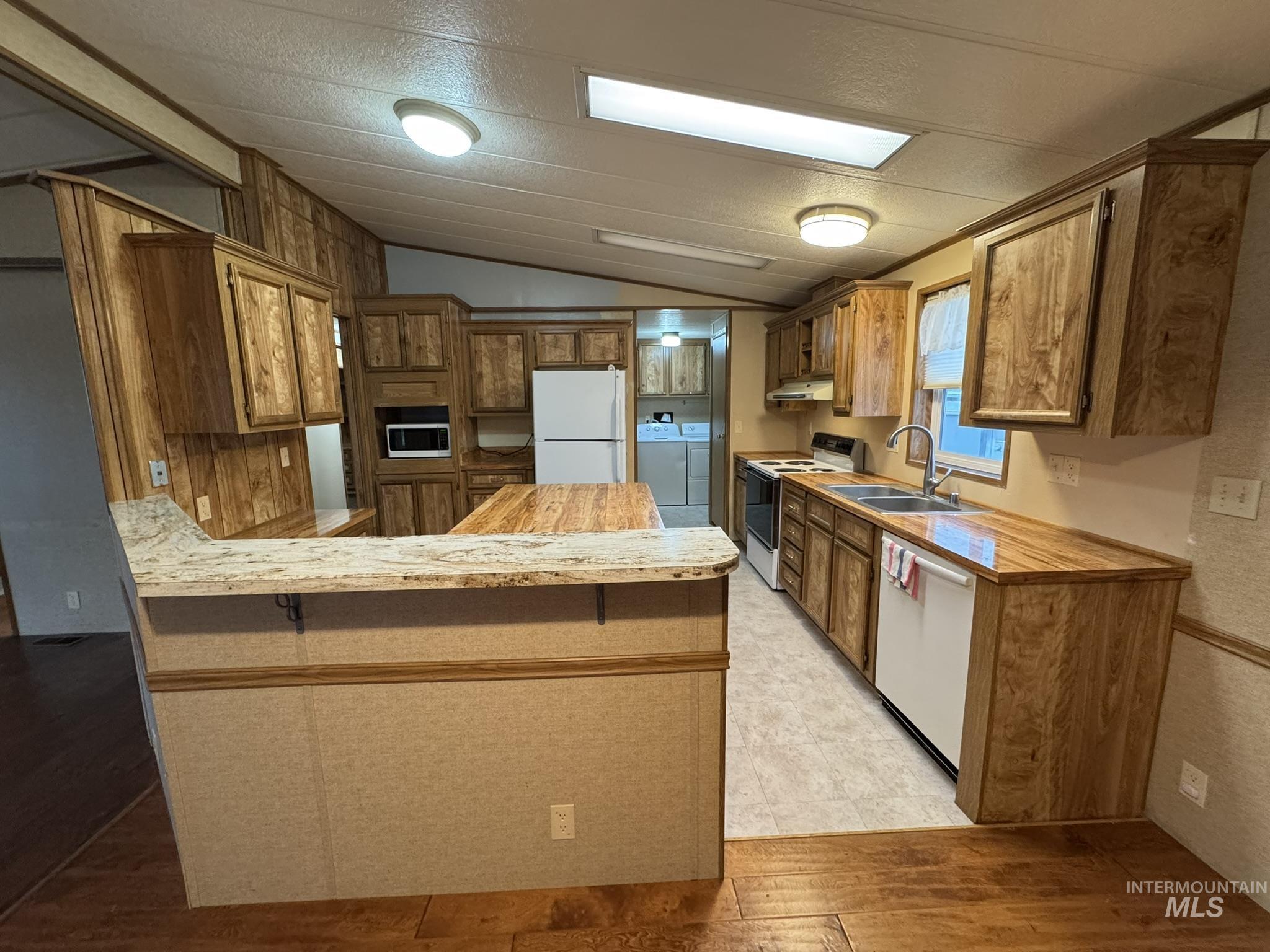 Kitchen featuring a peninsula, white appliances, vaulted ceiling, brown cabinets, and light wood-type flooring