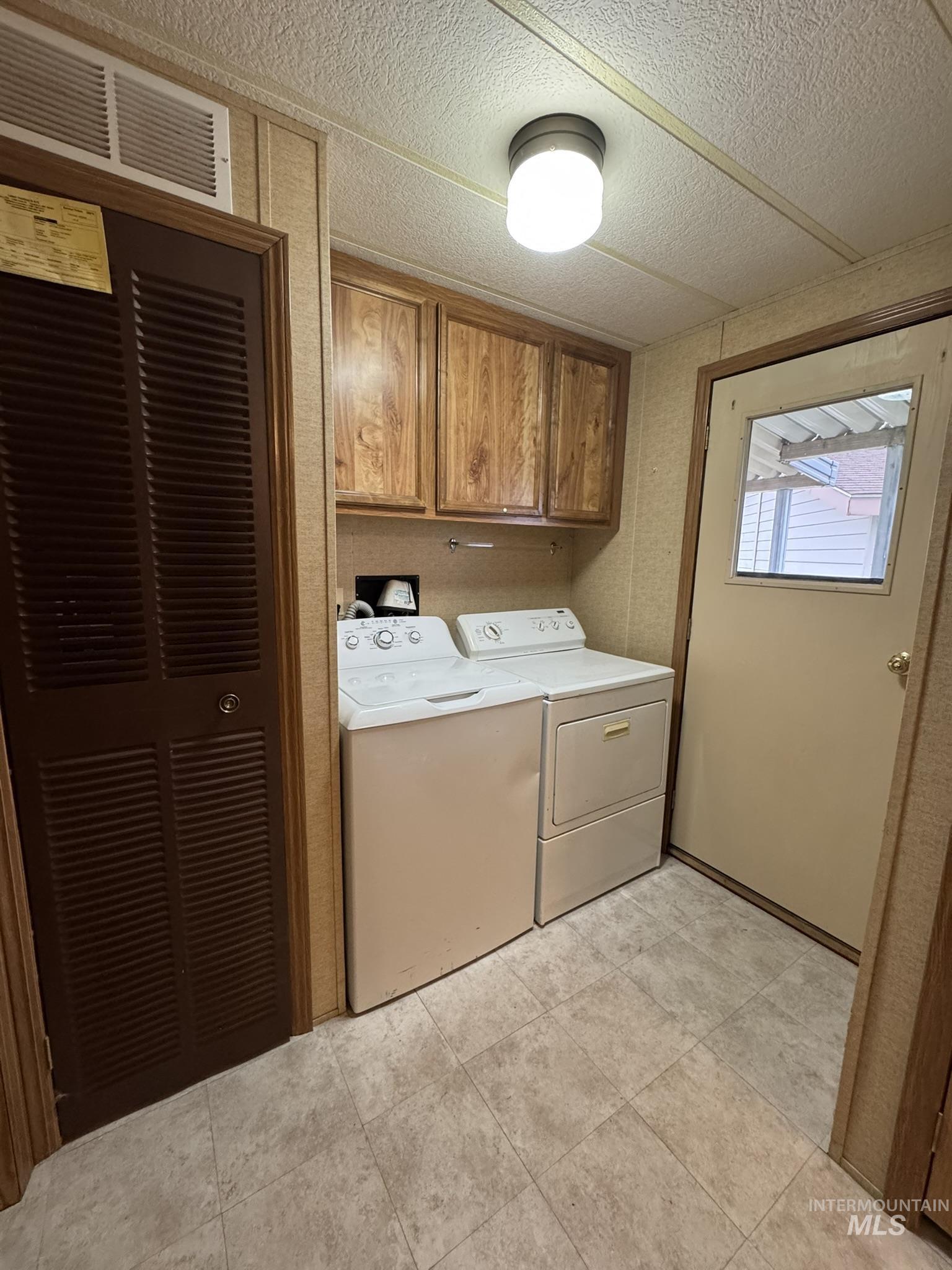 Laundry area featuring cabinet space, a heating unit, washing machine and clothes dryer, light tile patterned flooring, and a textured ceiling