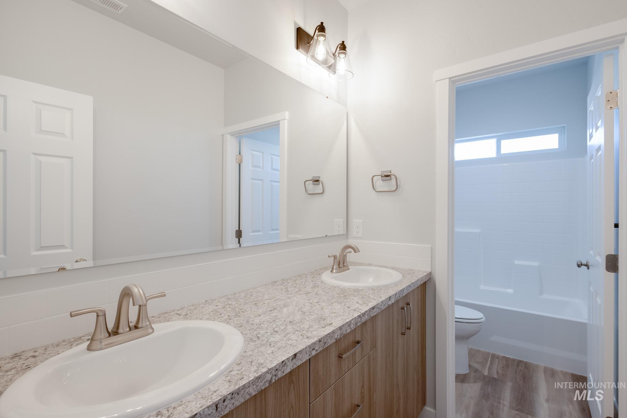 Full bathroom with double vanity, light wood-style flooring, and shower / bath combination