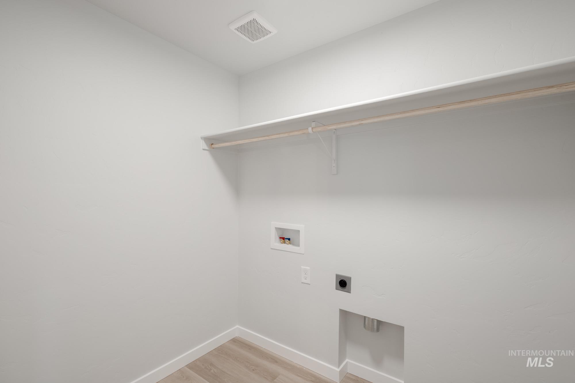 Washroom with light wood-type flooring, washer hookup, and hookup for an electric dryer