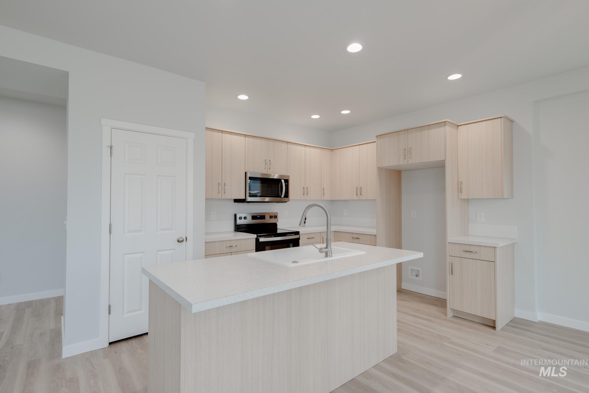 Kitchen featuring light brown cabinets, light countertops, recessed lighting, light wood finished floors, and appliances with stainless steel finishes