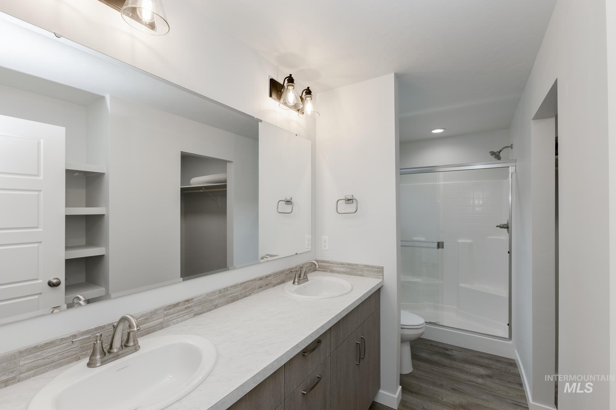 Bathroom with double vanity, a shower stall, dark wood finished floors, and a spacious closet