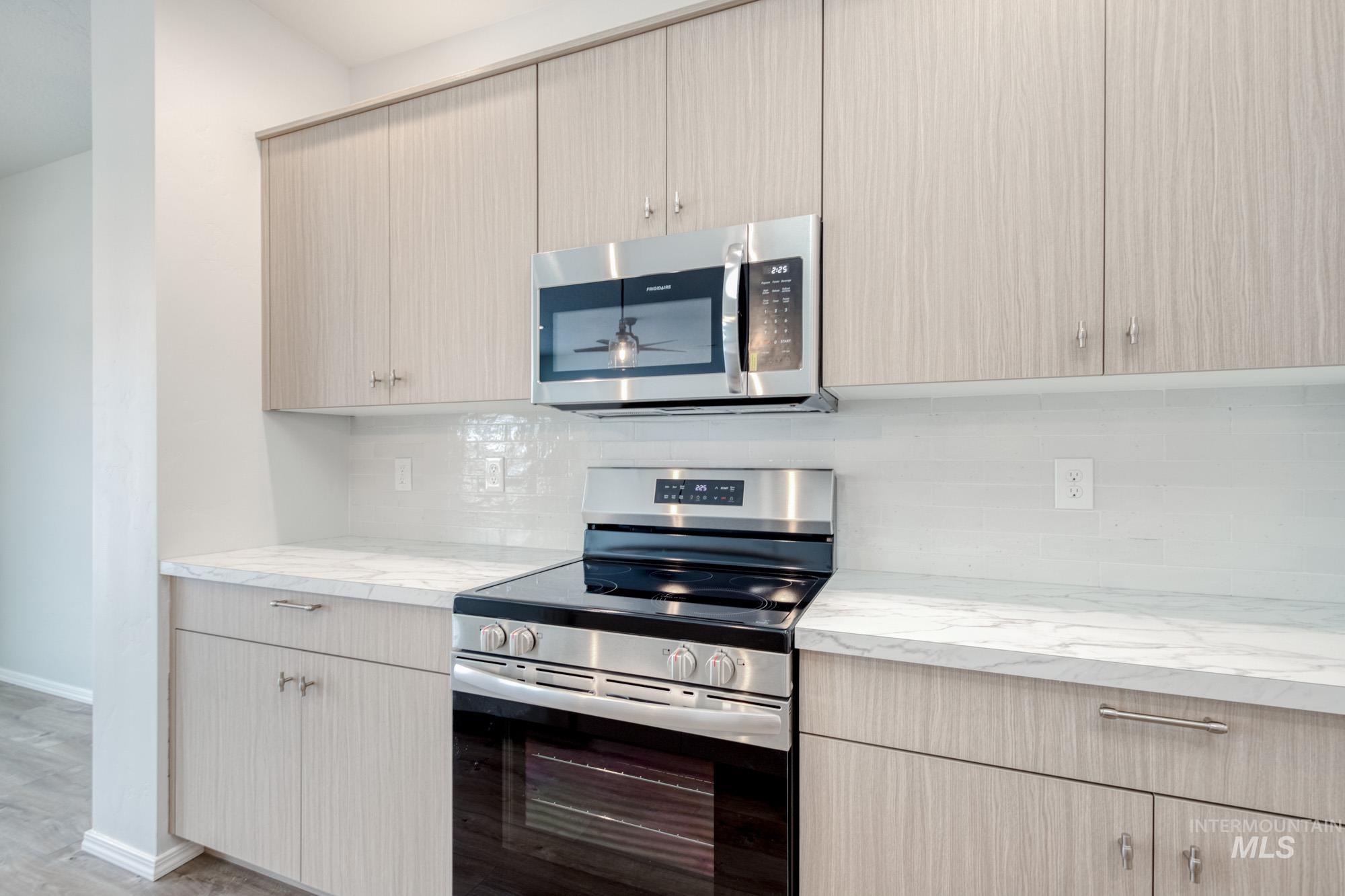 Kitchen featuring stainless steel appliances, tasteful backsplash, light stone countertops, and light brown cabinetry