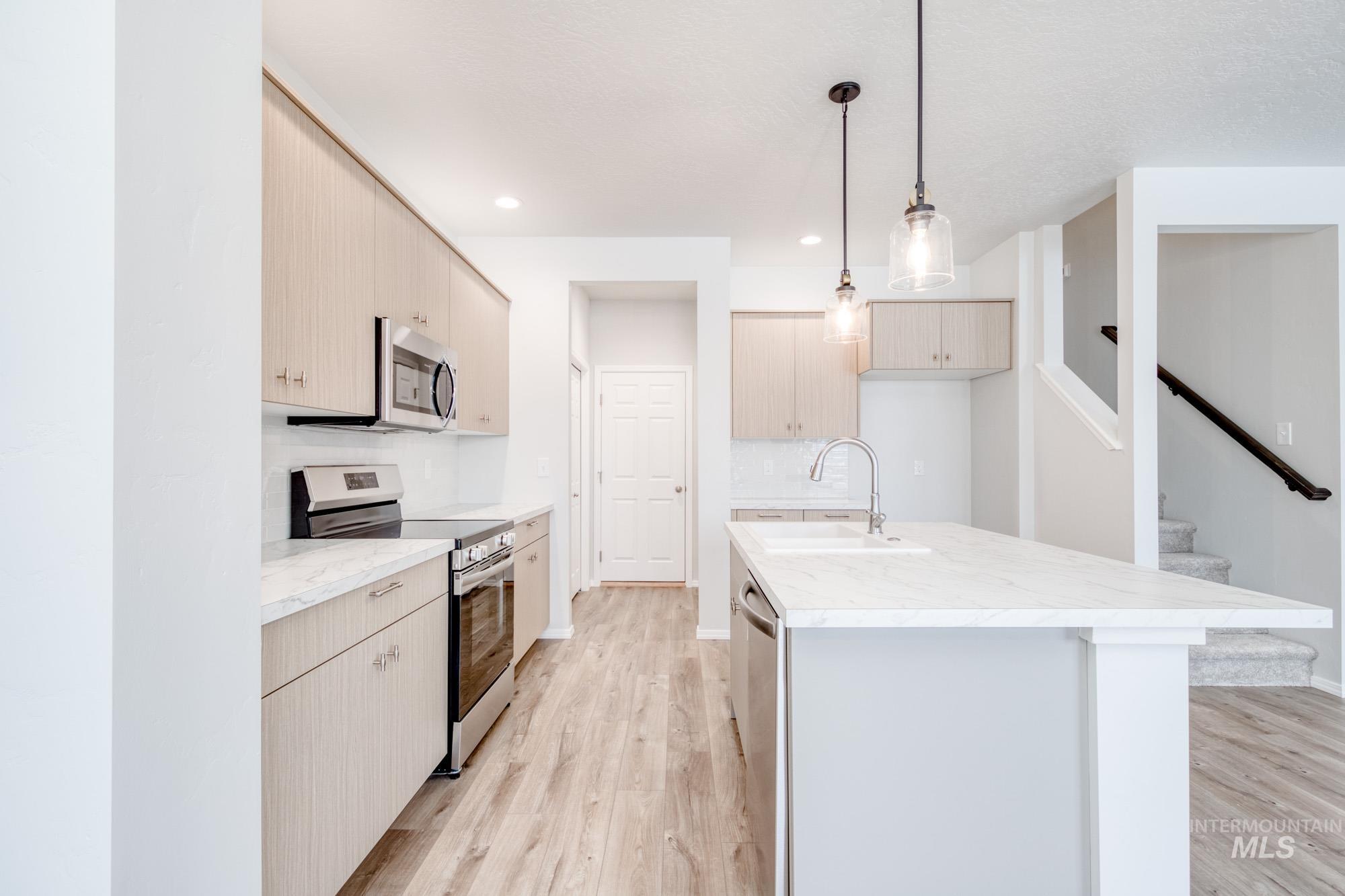 Kitchen with appliances with stainless steel finishes, decorative light fixtures, light wood-style flooring, an island with sink, and modern cabinets