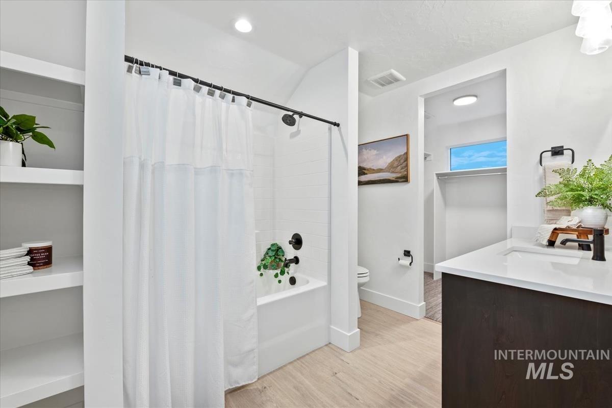 Bathroom featuring light wood-type flooring, vanity, shower / bath combination with curtain, and recessed lighting