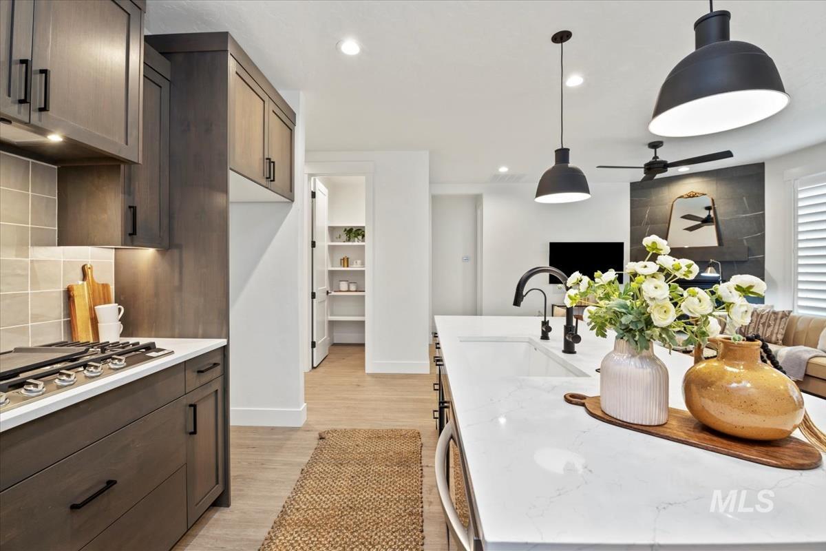 Kitchen with light stone counters, hanging light fixtures, dark brown cabinets, light wood-style flooring, and recessed lighting