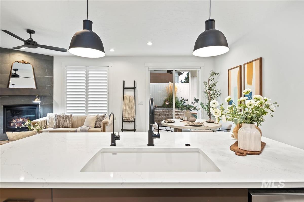 Kitchen with hanging light fixtures, a kitchen island with sink, light stone counters, open floor plan, and a large fireplace