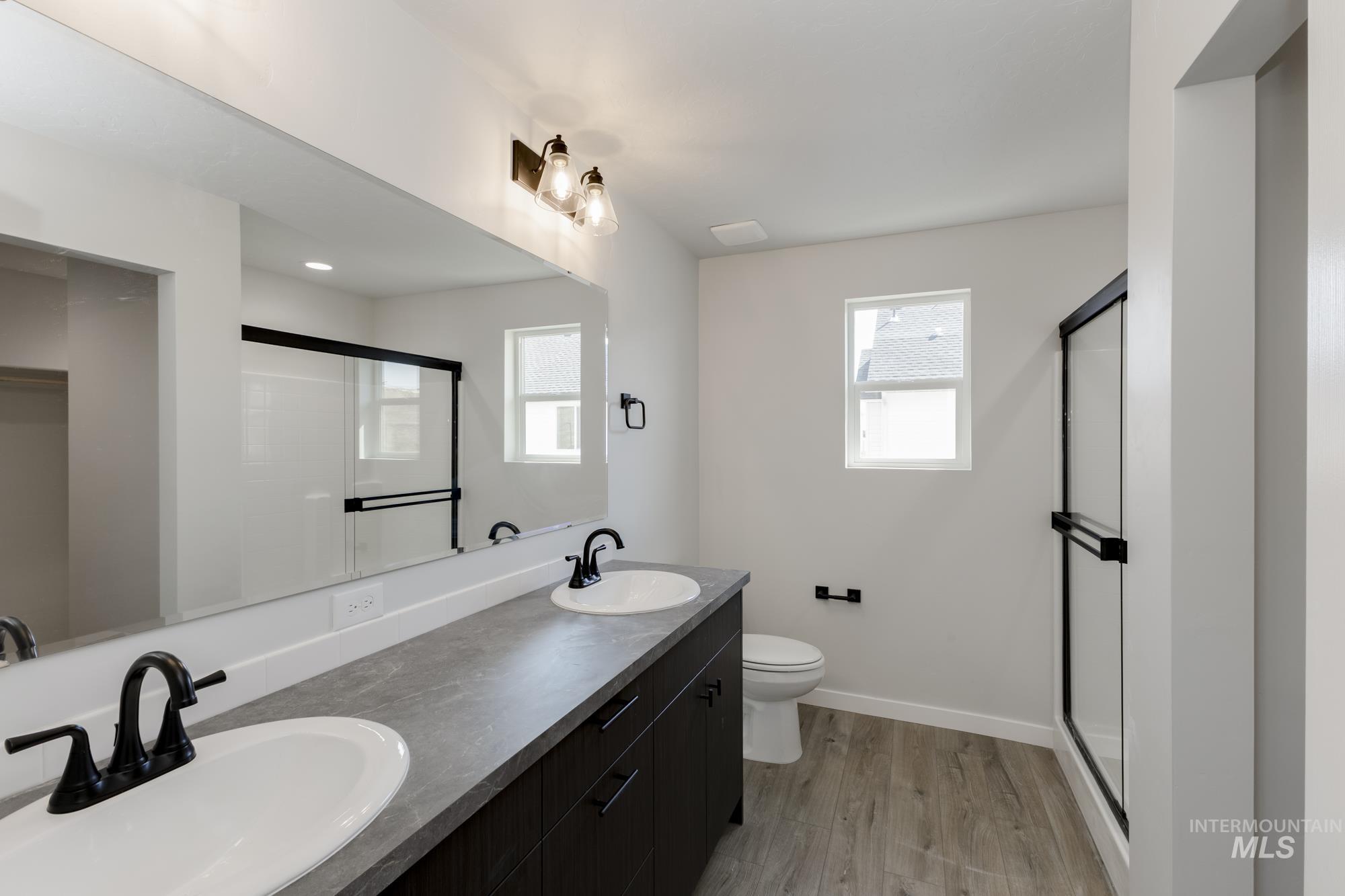 Bathroom with double vanity, a shower stall, light wood-style flooring, and plenty of natural light