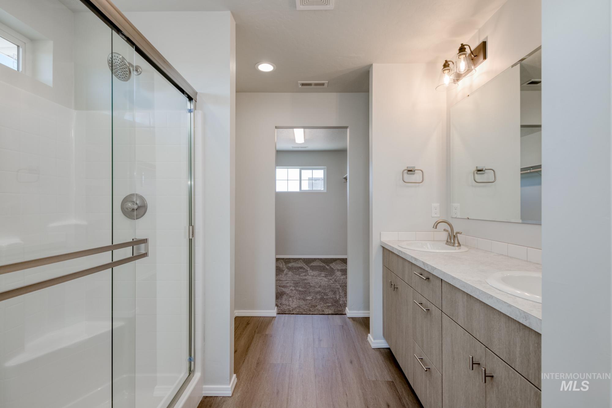 Bathroom featuring double vanity, a shower stall, light wood-style flooring, and recessed lighting