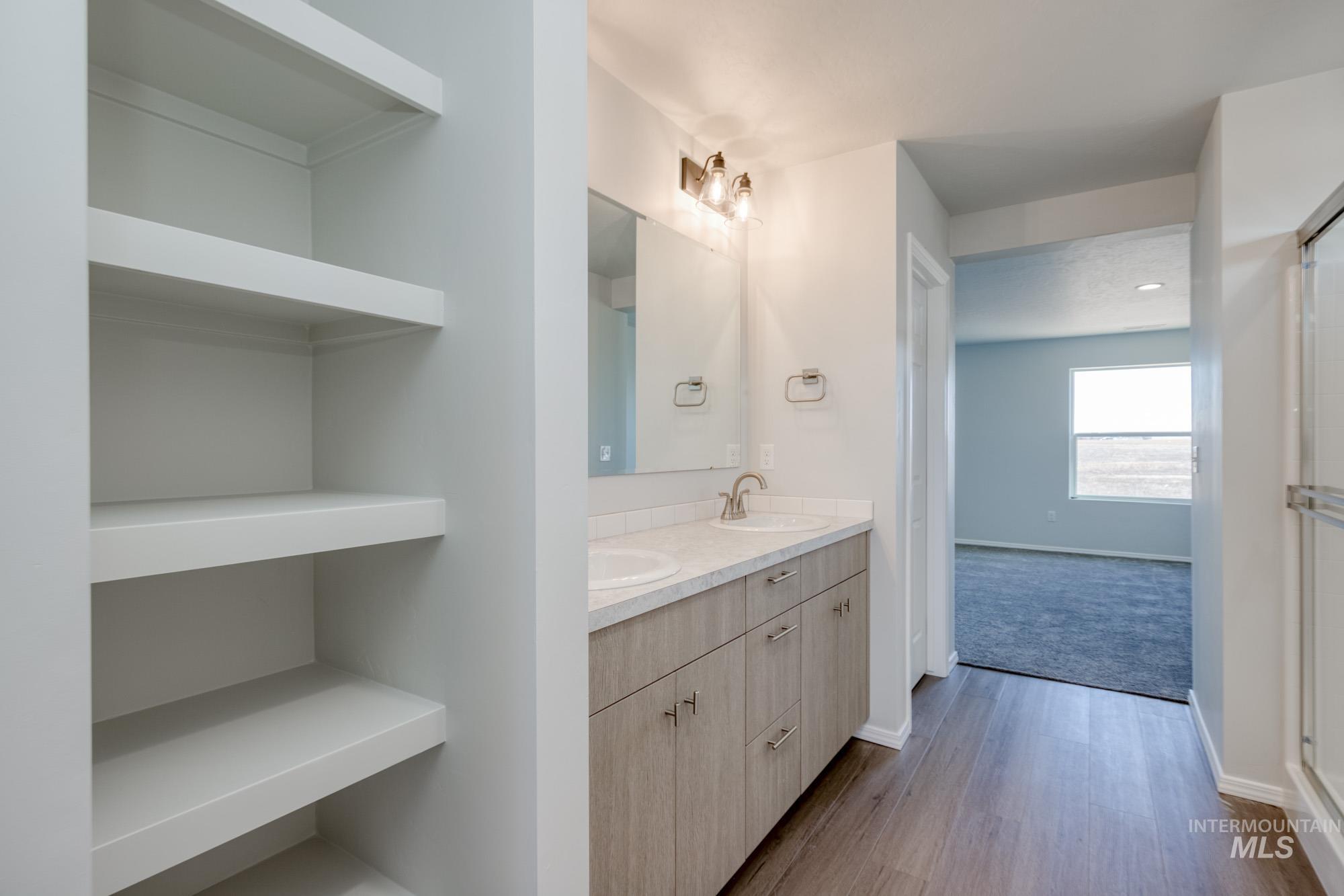Full bath with double vanity, light wood-style flooring, and an enclosed shower