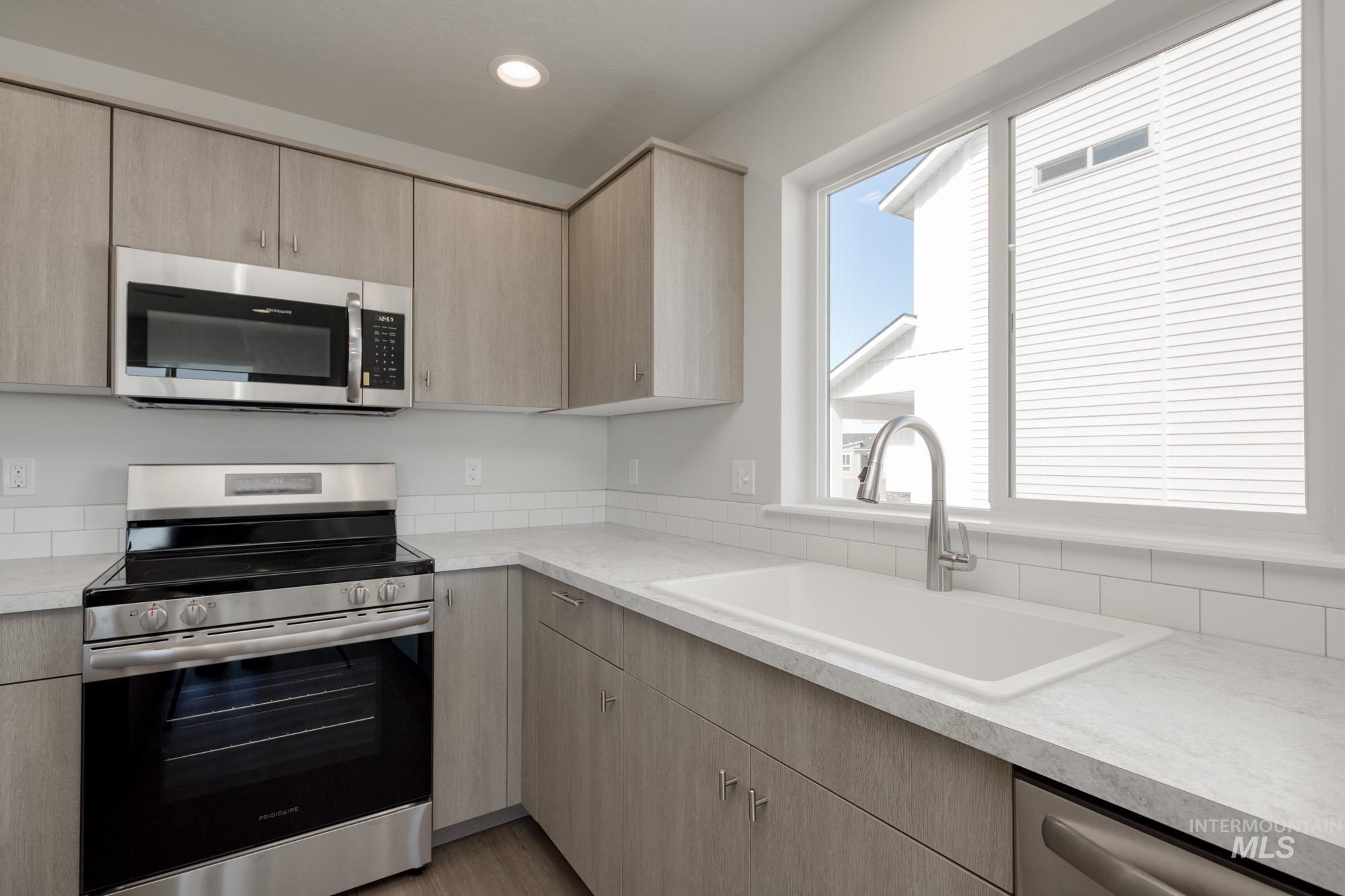 Kitchen with stainless steel appliances, light brown cabinets, light countertops, and recessed lighting