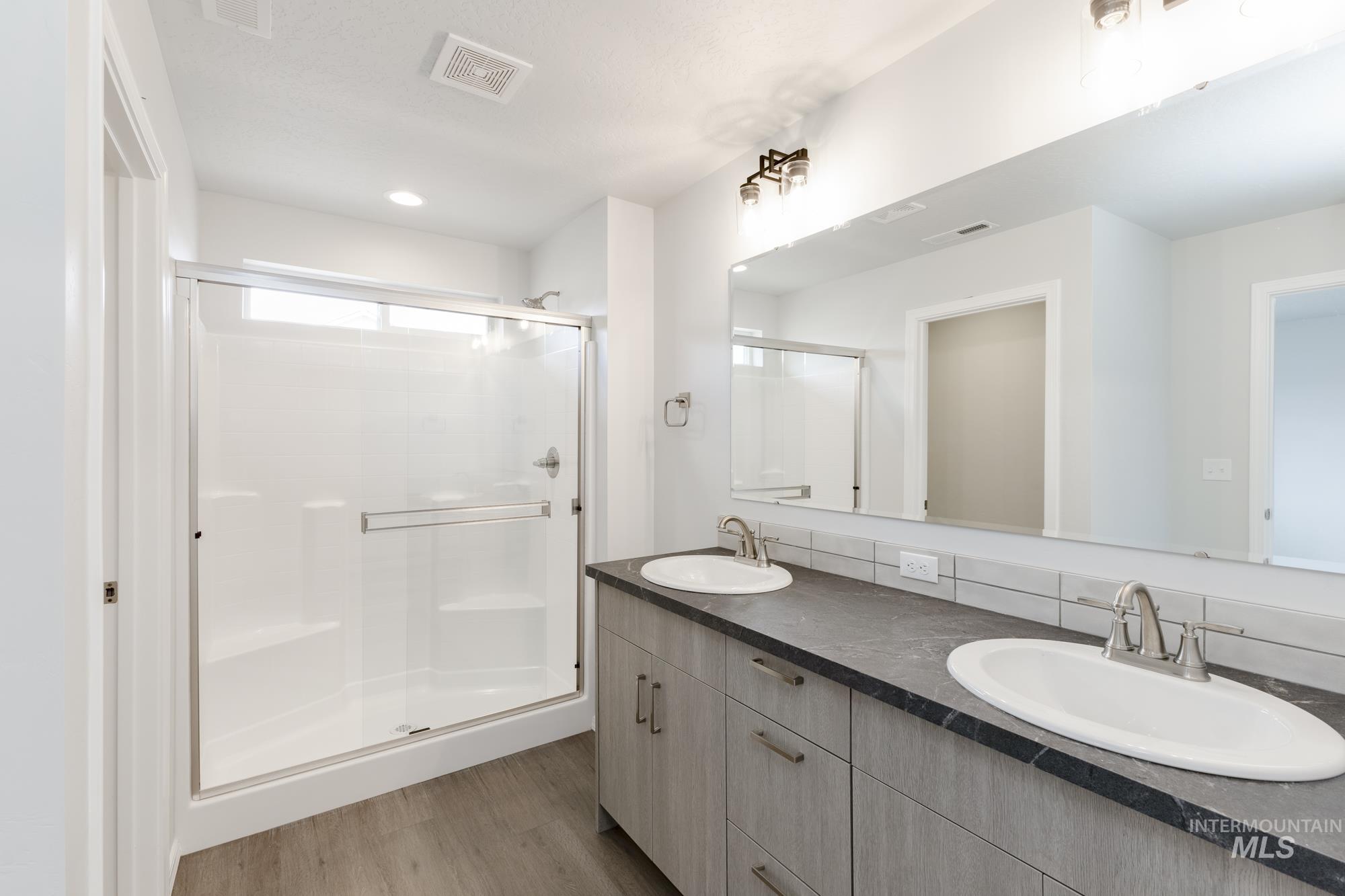 Full bath with double vanity, light wood-style flooring, a shower stall, and recessed lighting