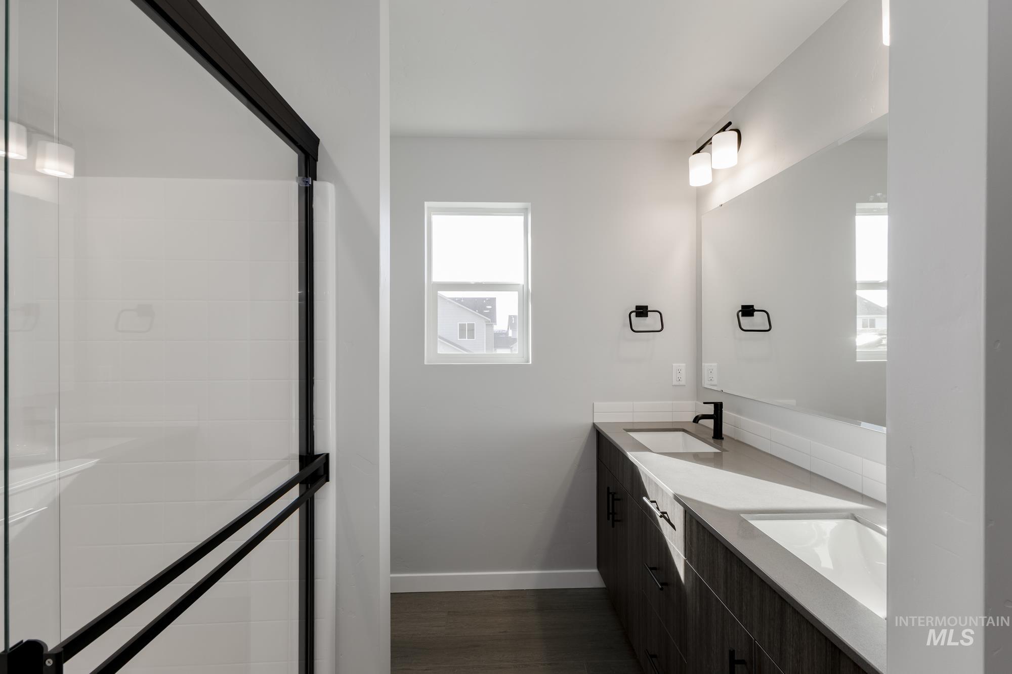 Bathroom with double vanity, a stall shower, and dark wood-style floors