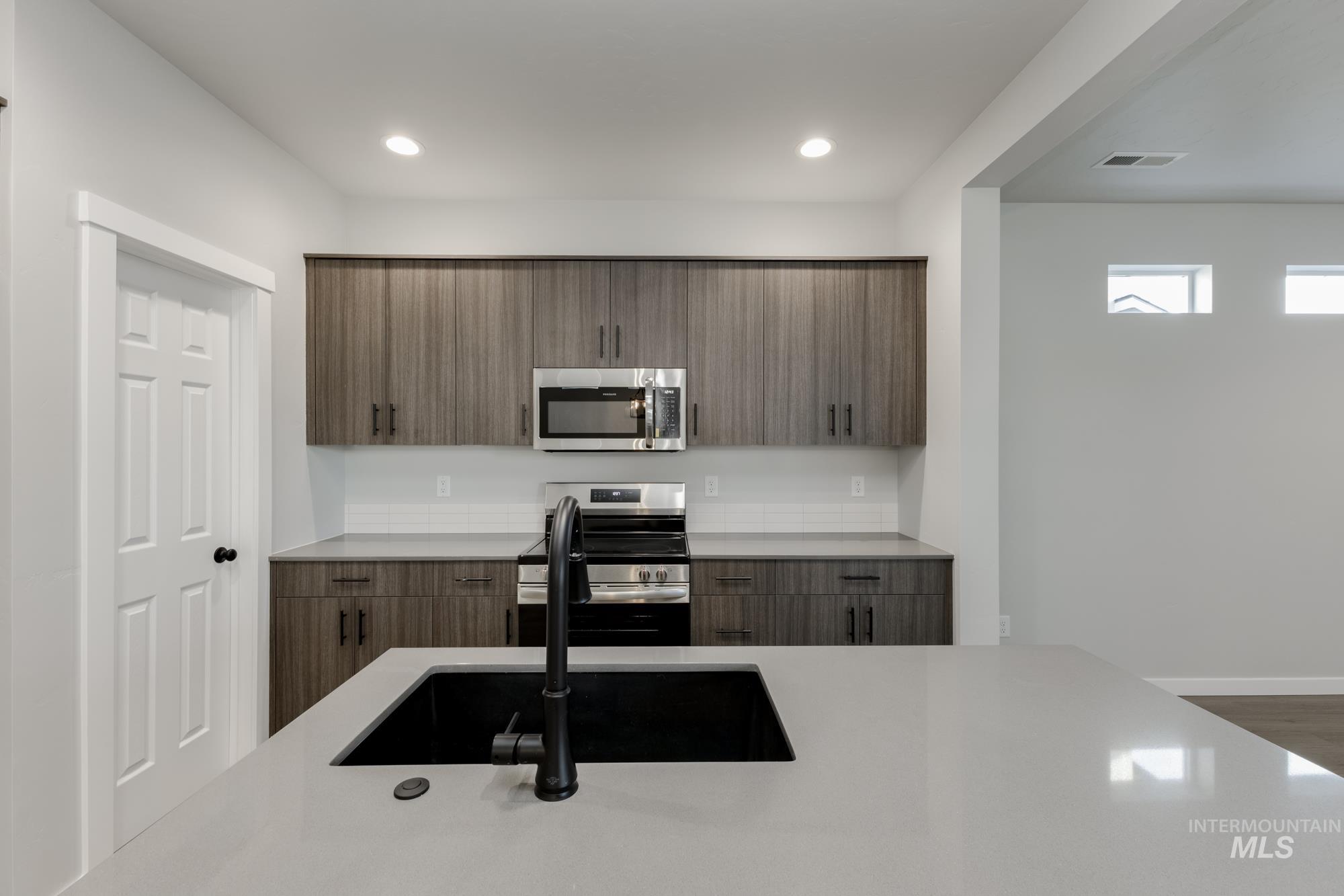 Kitchen with modern cabinets, appliances with stainless steel finishes, light stone counters, and recessed lighting