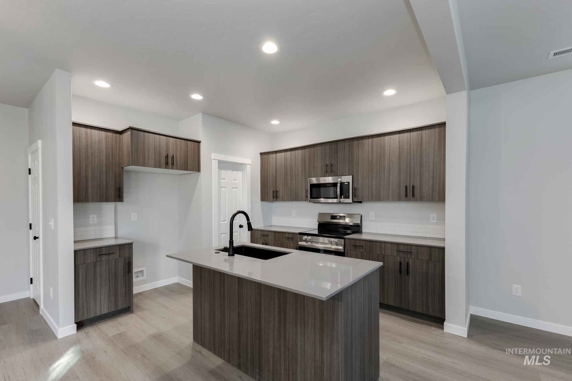 Kitchen featuring appliances with stainless steel finishes, modern cabinets, light wood-style floors, an island with sink, and recessed lighting