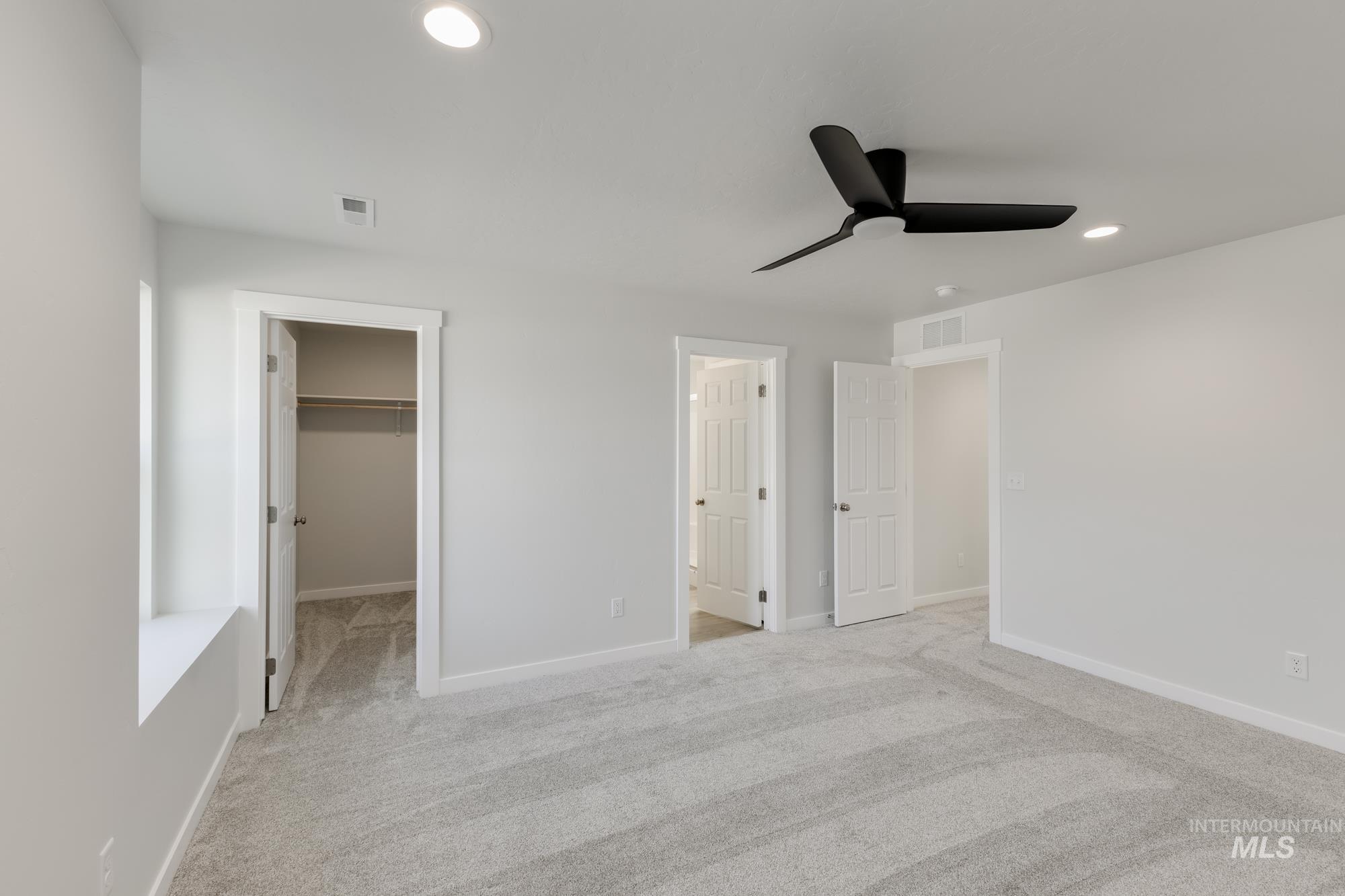 Unfurnished bedroom with a spacious closet, light carpet, recessed lighting, ceiling fan, and ensuite bath