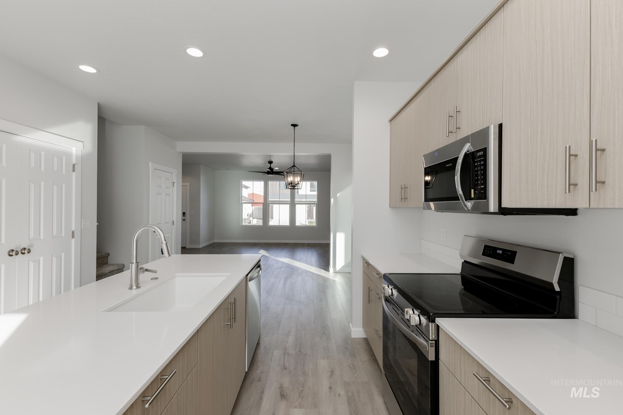Kitchen featuring stainless steel appliances, modern cabinets, light wood-style floors, light brown cabinetry, and decorative light fixtures