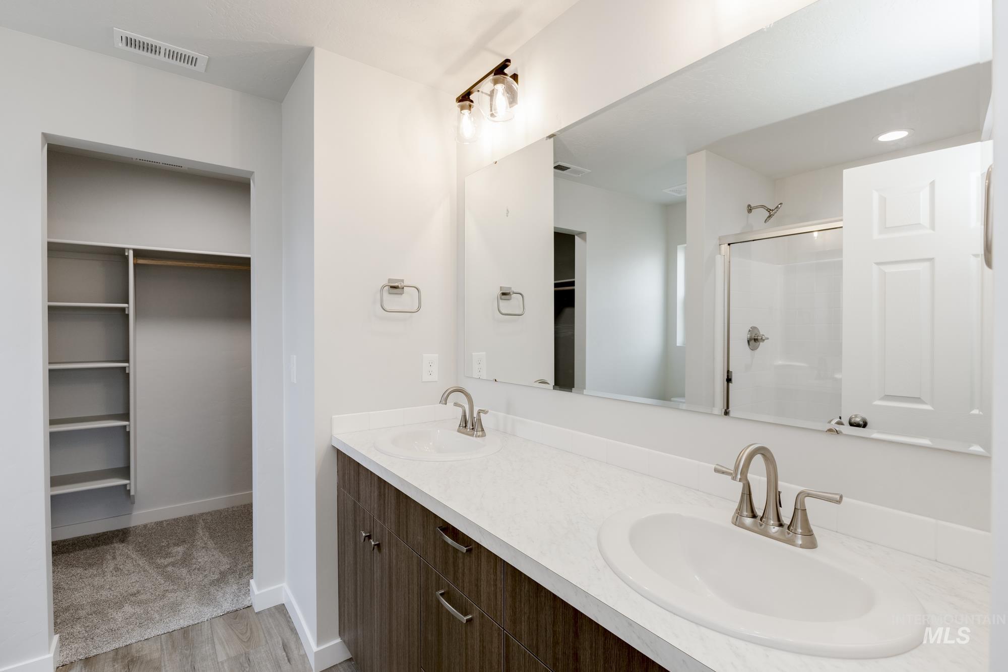 Bathroom featuring a spacious closet, a stall shower, double vanity, and light wood-type flooring