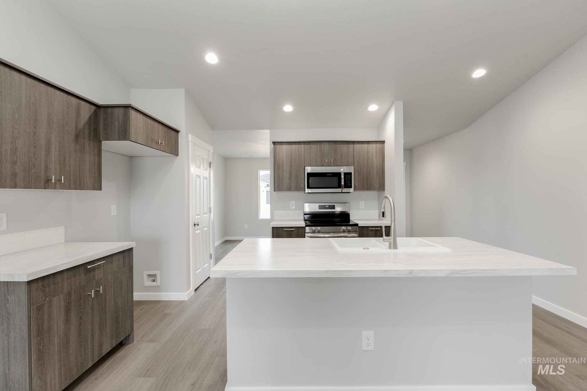Kitchen featuring stainless steel appliances, light wood finished floors, modern cabinets, recessed lighting, and an island with sink