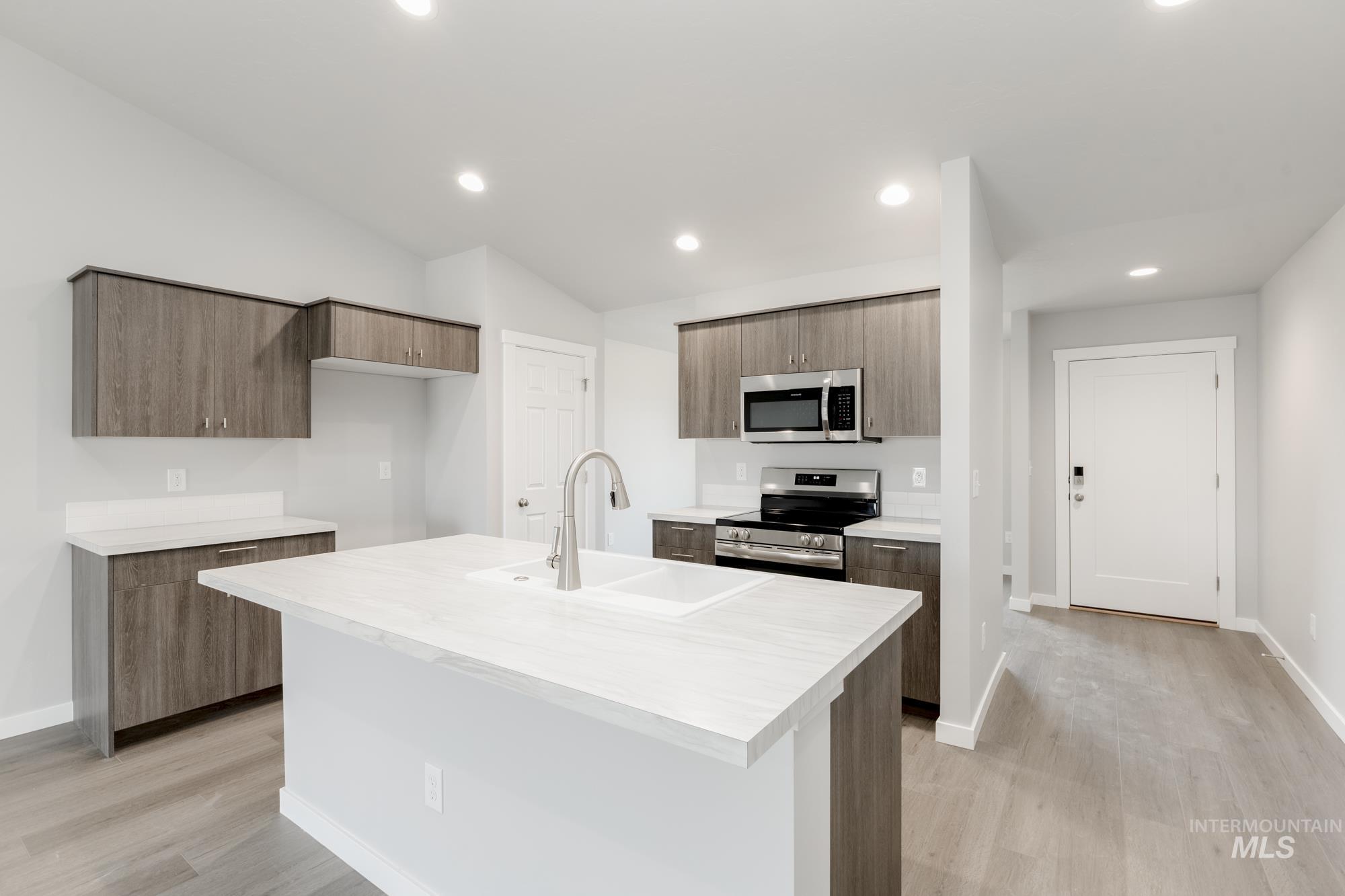 Kitchen with light countertops, appliances with stainless steel finishes, light wood-type flooring, modern cabinets, and an island with sink