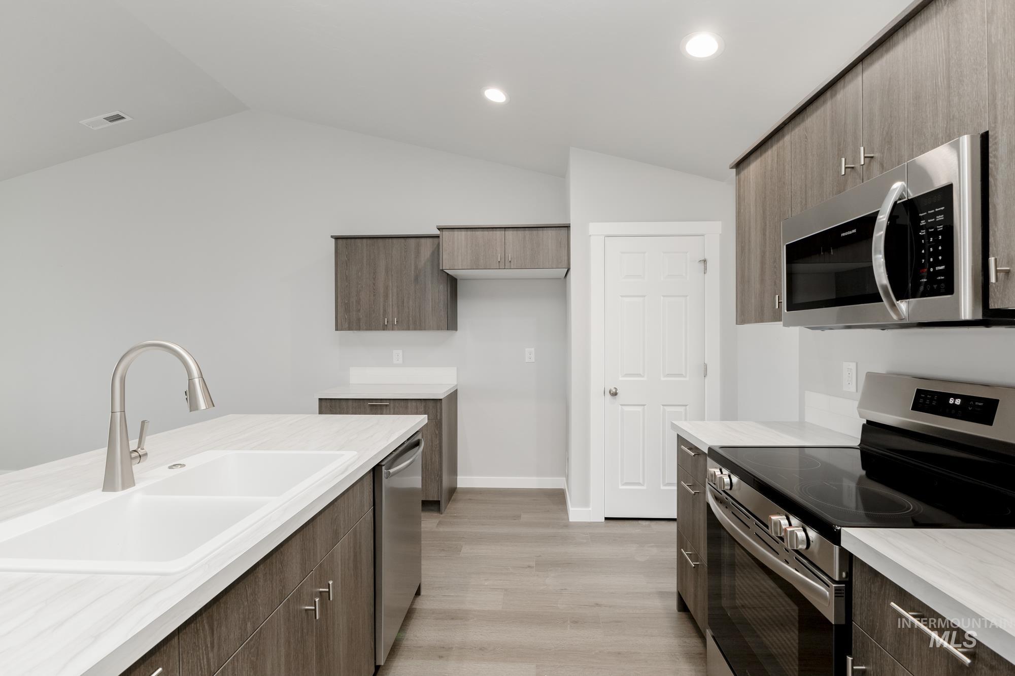 Kitchen featuring appliances with stainless steel finishes, modern cabinets, light wood-style flooring, vaulted ceiling, and recessed lighting