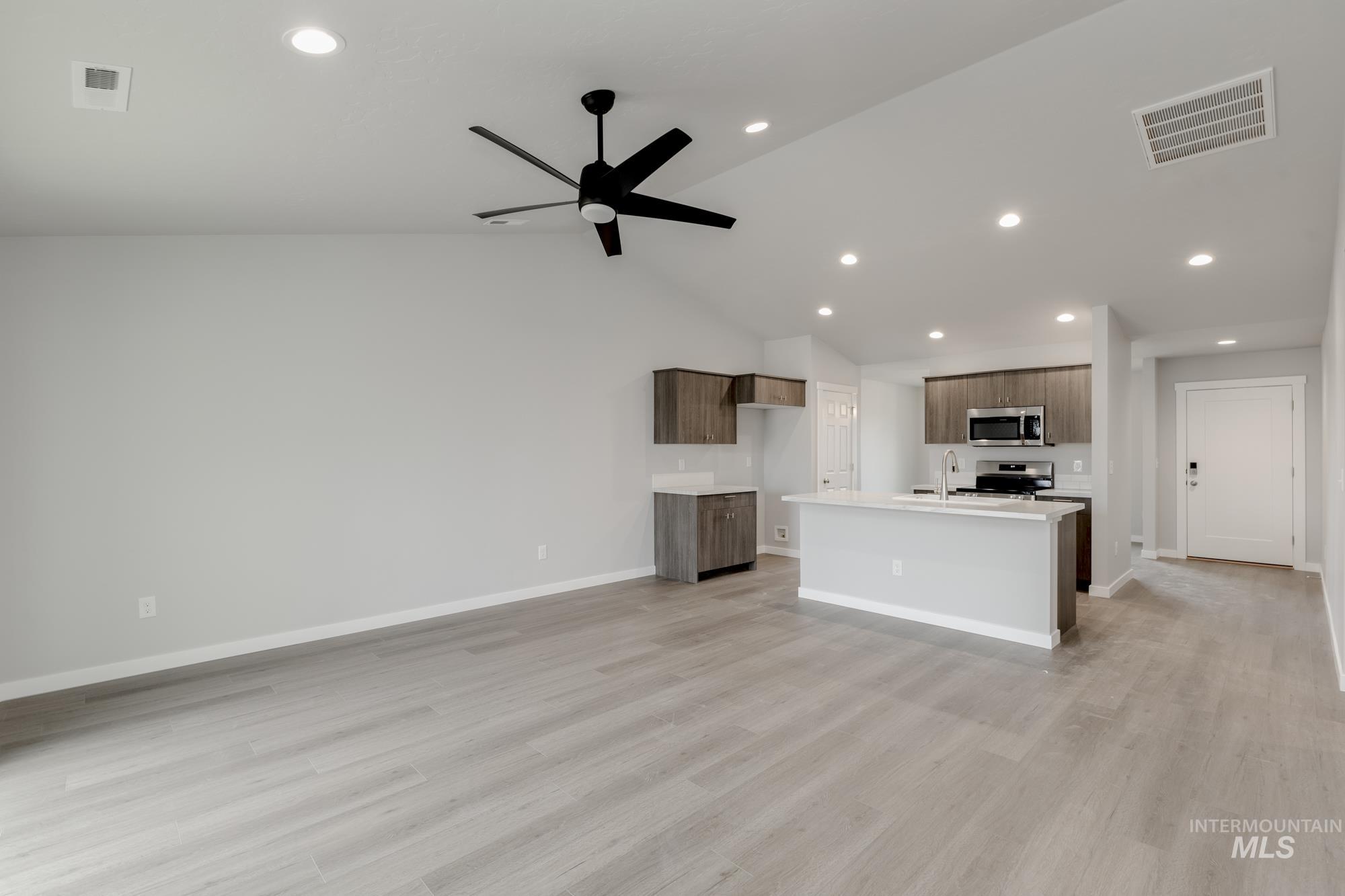 Kitchen featuring recessed lighting, open floor plan, an island with sink, light wood-style floors, and vaulted ceiling