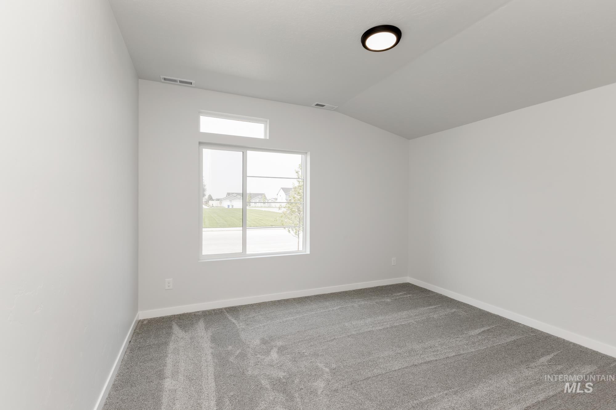 Carpeted empty room featuring vaulted ceiling and baseboards