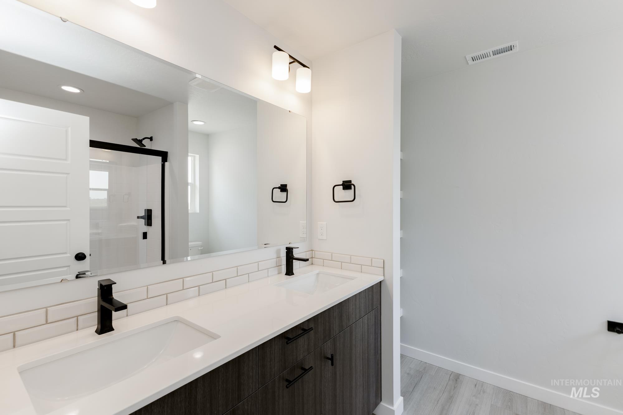 Bathroom with double vanity, a shower stall, light wood-style flooring, and recessed lighting