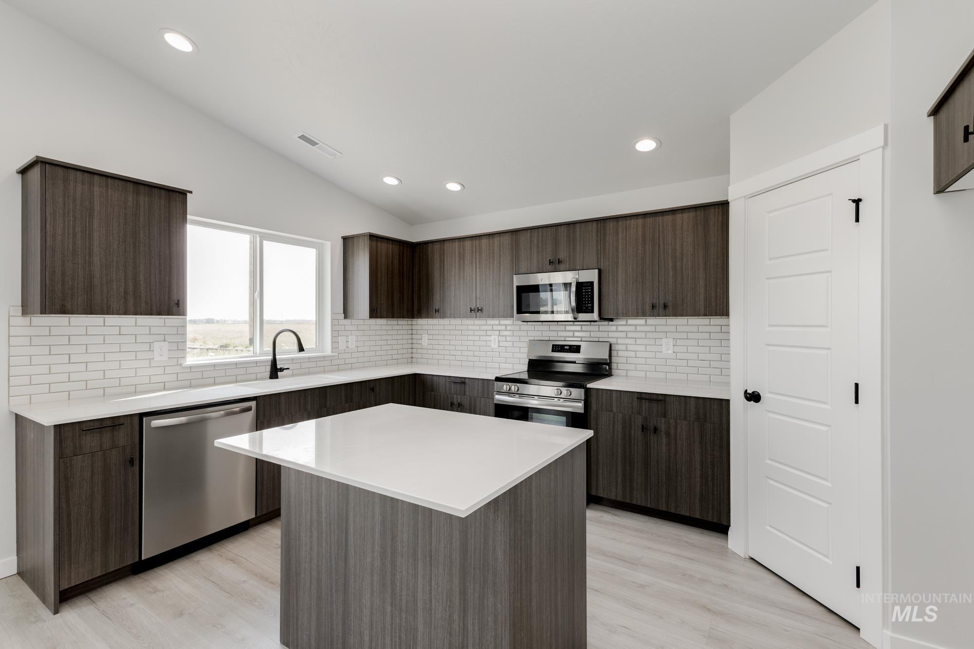 Kitchen featuring backsplash, modern cabinets, stainless steel appliances, dark brown cabinets, and lofted ceiling