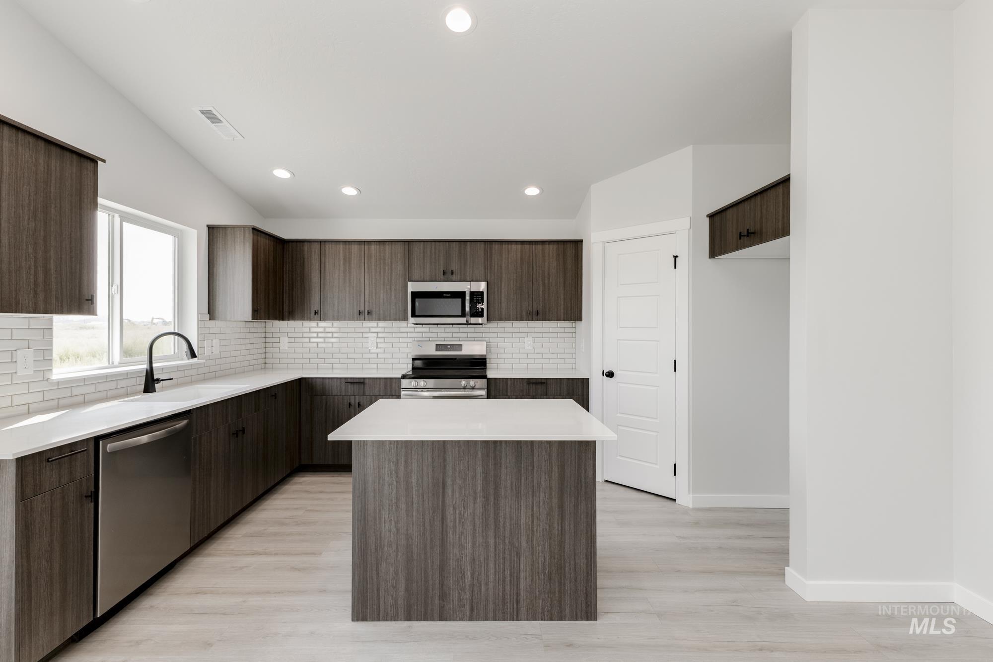 Kitchen with backsplash, modern cabinets, a kitchen island, dark brown cabinets, and appliances with stainless steel finishes