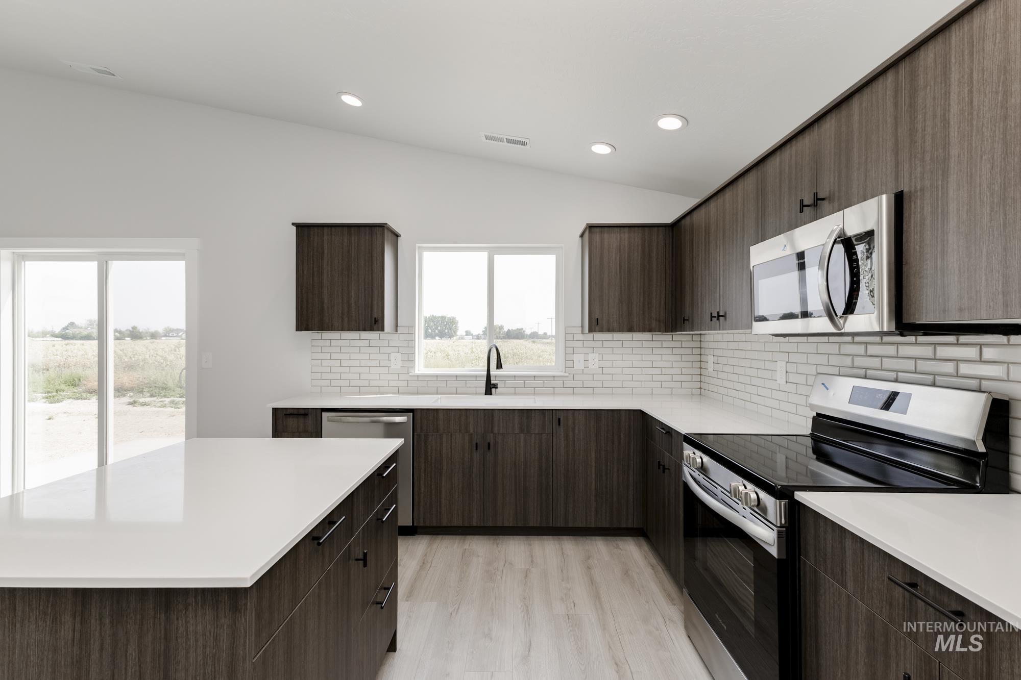 Kitchen featuring appliances with stainless steel finishes, vaulted ceiling, tasteful backsplash, dark brown cabinetry, and light wood-style flooring