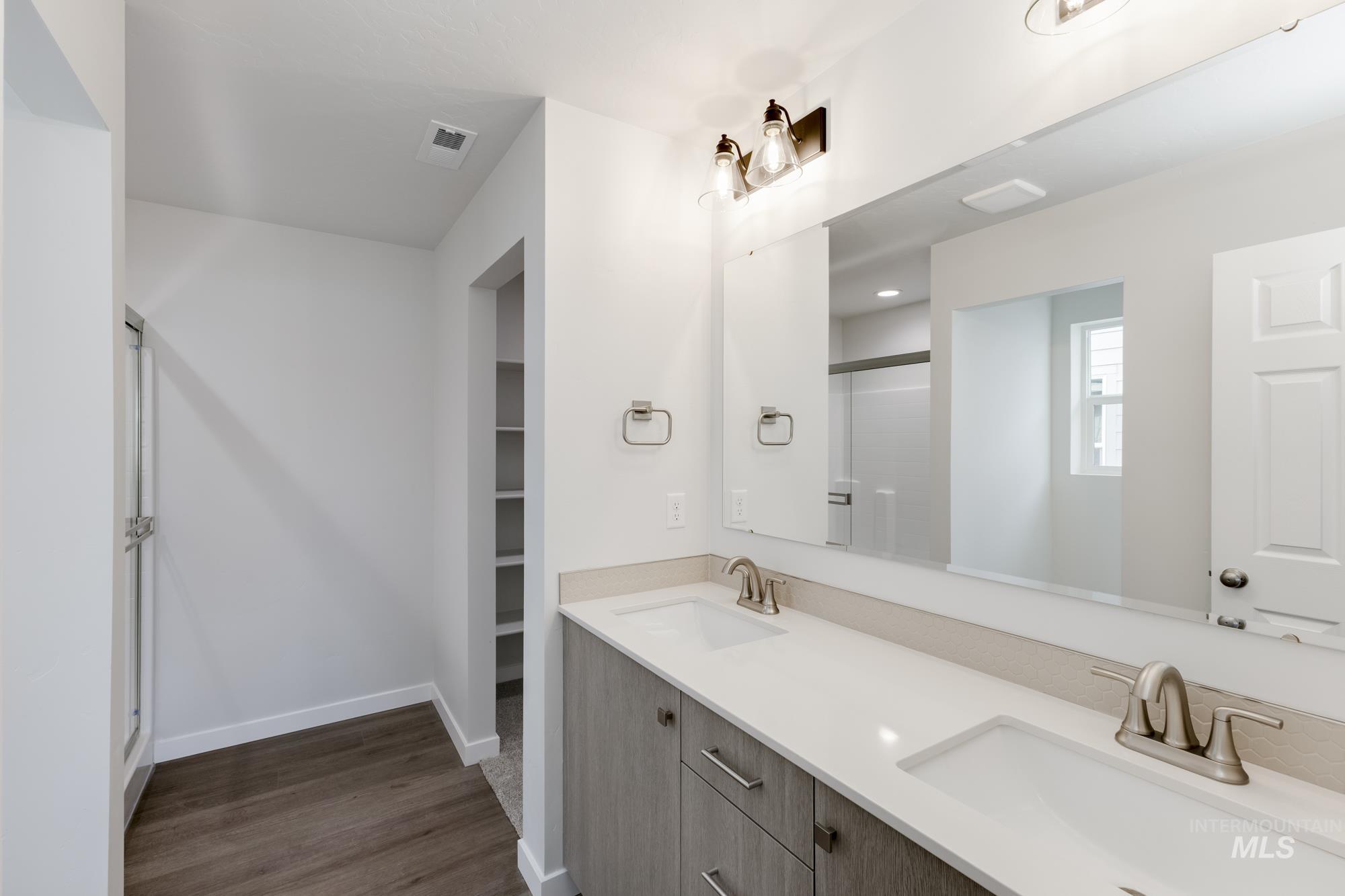 Bathroom with a shower stall, double vanity, a spacious closet, and dark wood-style flooring