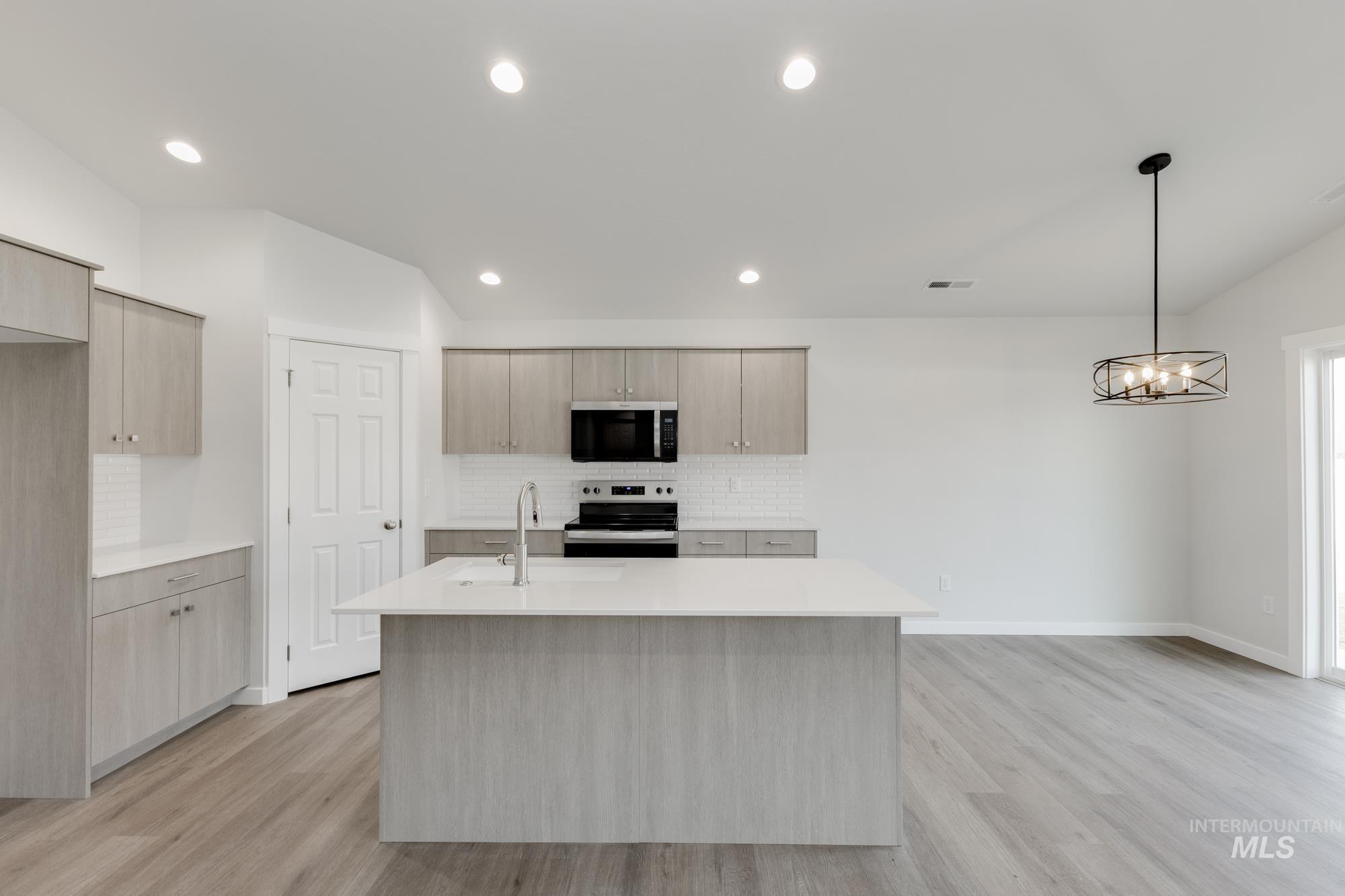 Kitchen with an island with sink, appliances with stainless steel finishes, tasteful backsplash, hanging light fixtures, and vaulted ceiling
