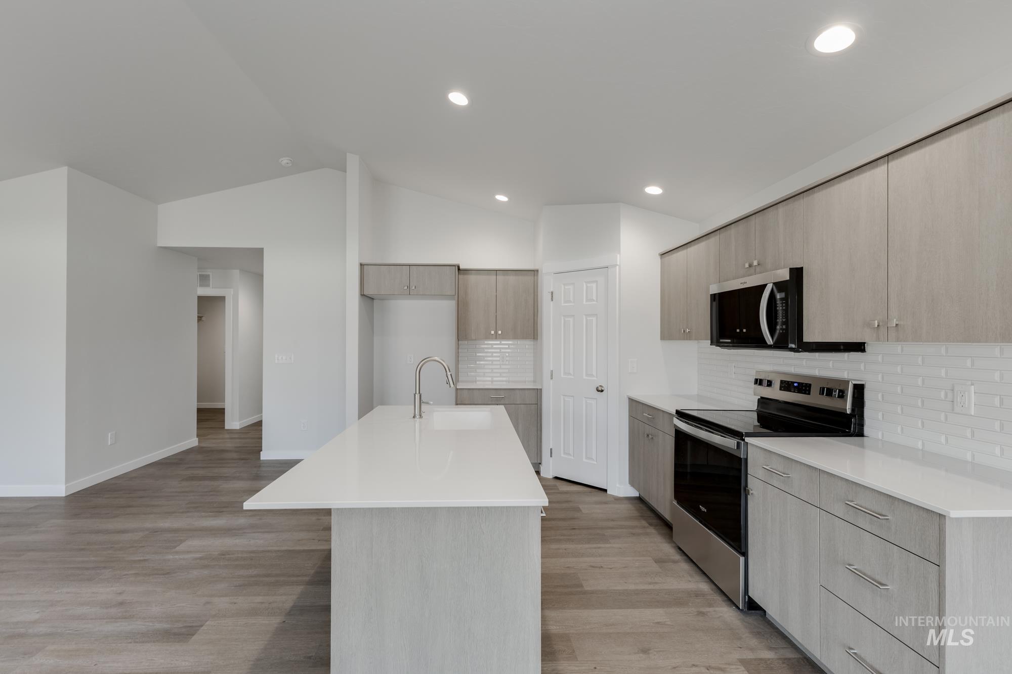 Kitchen featuring appliances with stainless steel finishes, tasteful backsplash, modern cabinets, an island with sink, and light wood-style floors