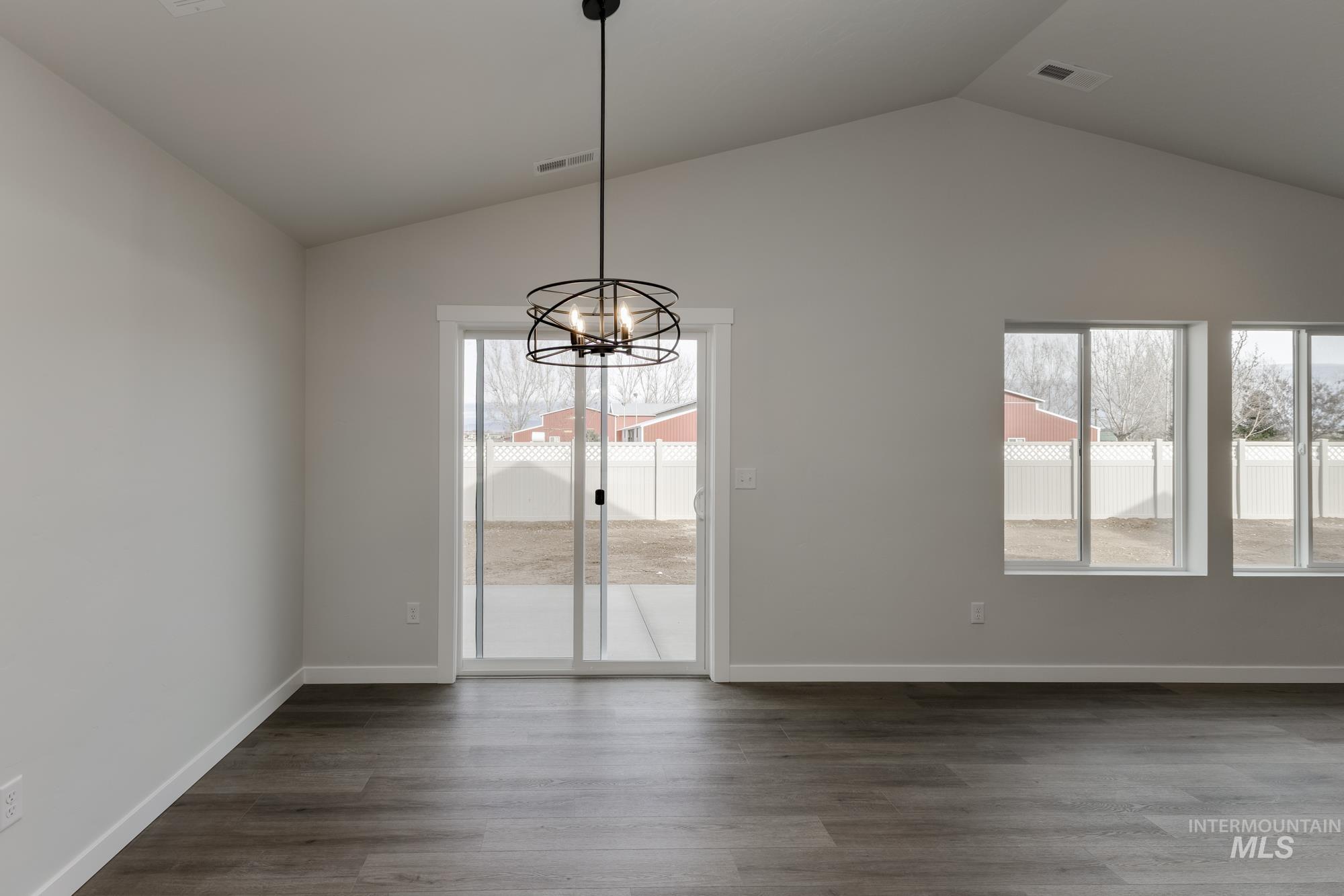 Unfurnished dining area with lofted ceiling, dark wood-style floors, healthy amount of natural light, and a chandelier