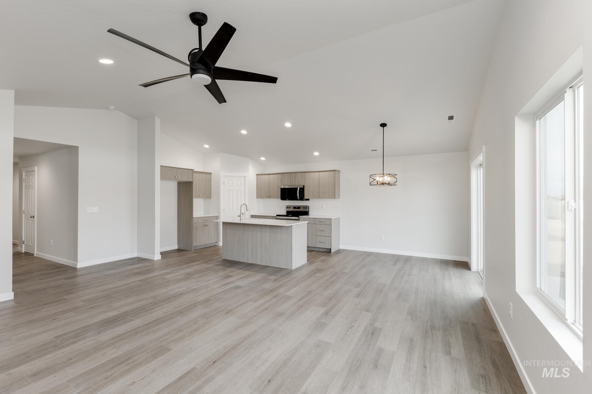 Kitchen featuring open floor plan, vaulted ceiling, light countertops, an island with sink, and a ceiling fan