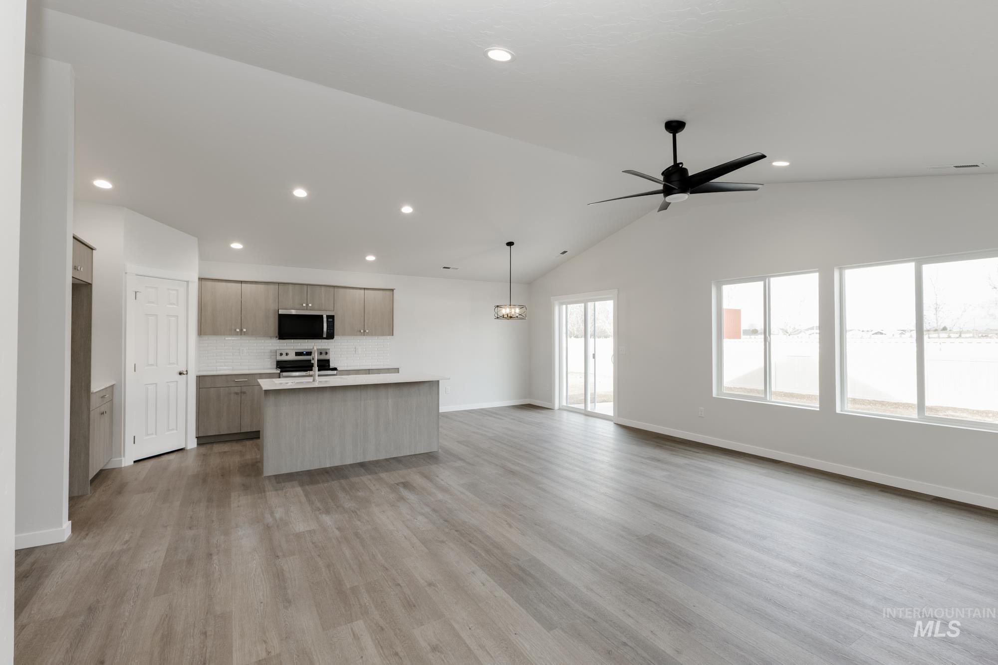 Kitchen featuring open floor plan, light countertops, an island with sink, vaulted ceiling, and backsplash