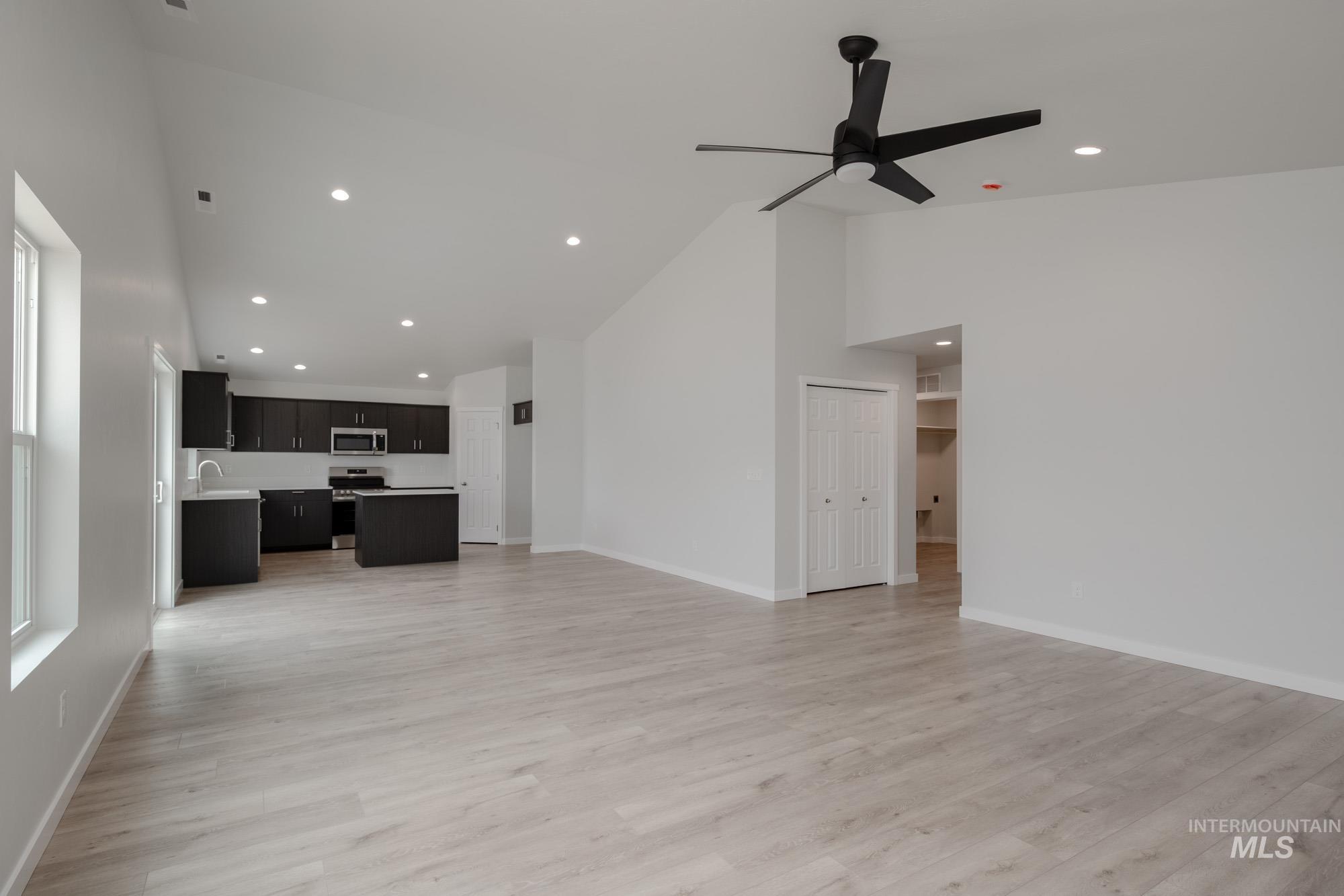 Unfurnished living room with high vaulted ceiling, light wood-type flooring, and recessed lighting