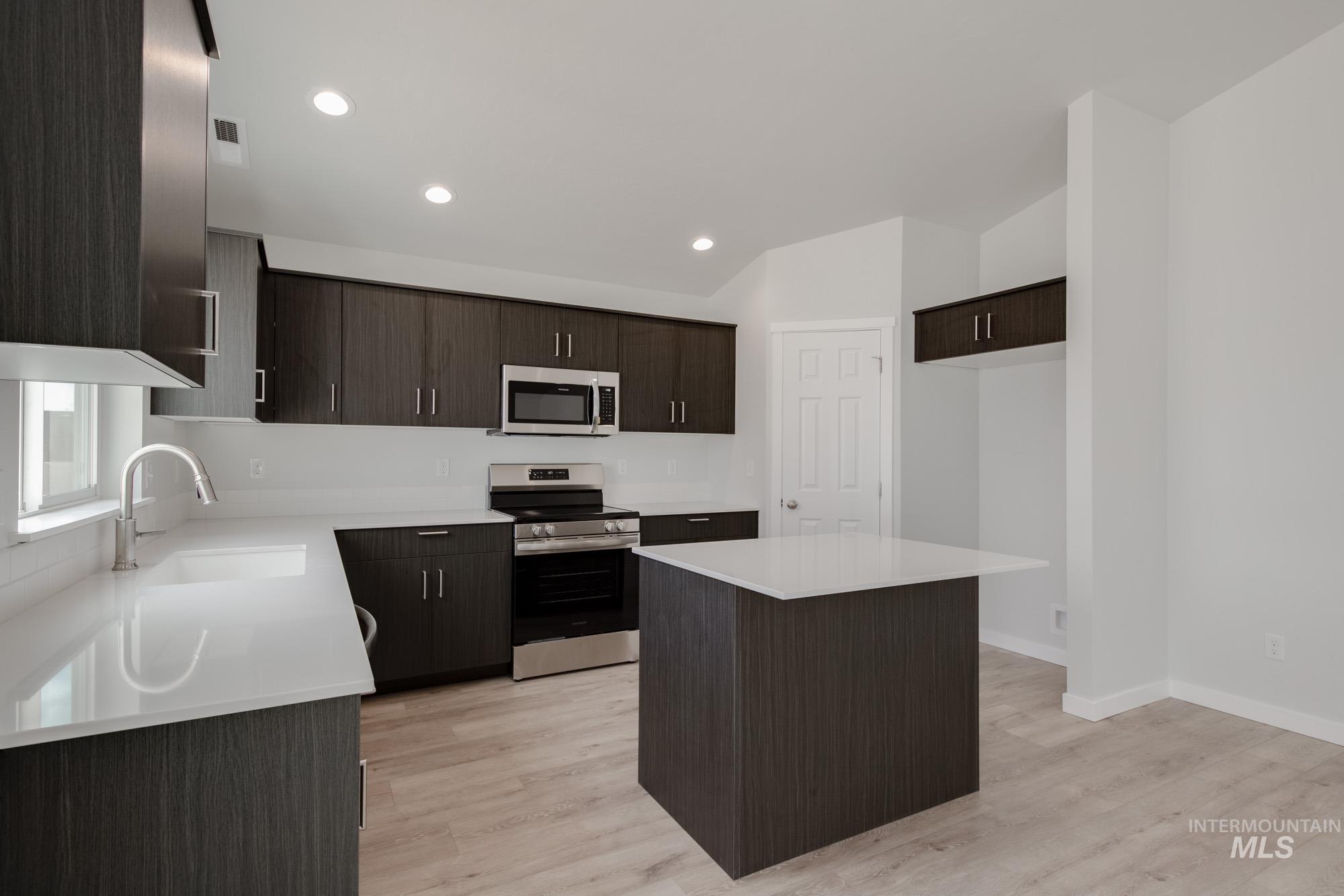 Kitchen with dark brown cabinetry, appliances with stainless steel finishes, a center island, light wood-style flooring, and recessed lighting