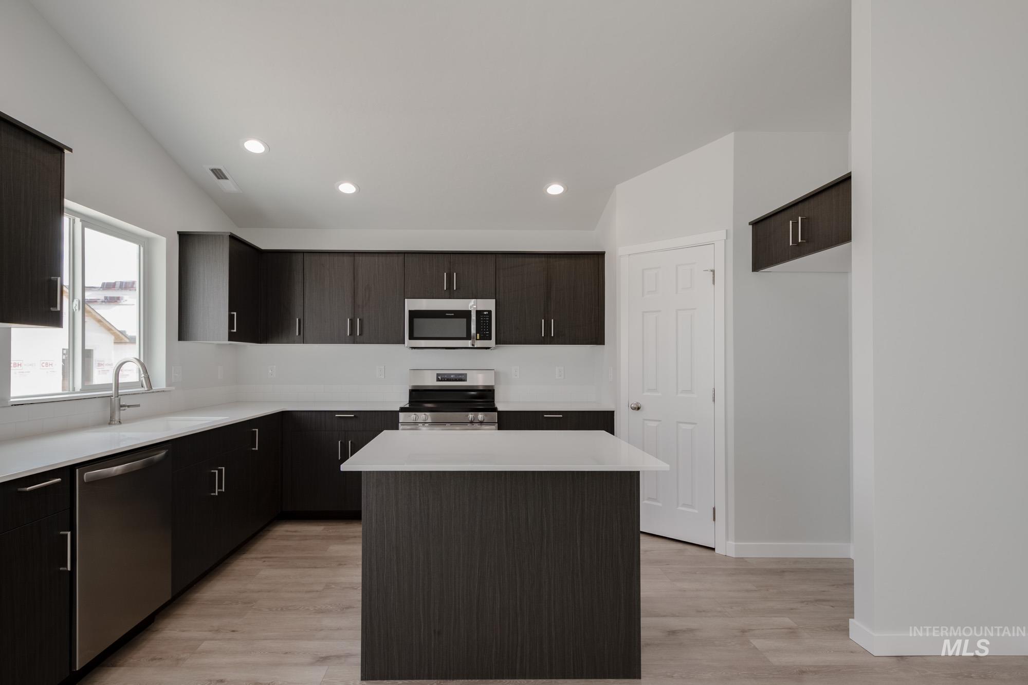 Kitchen with a kitchen island, appliances with stainless steel finishes, recessed lighting, light wood-style flooring, and dark brown cabinets