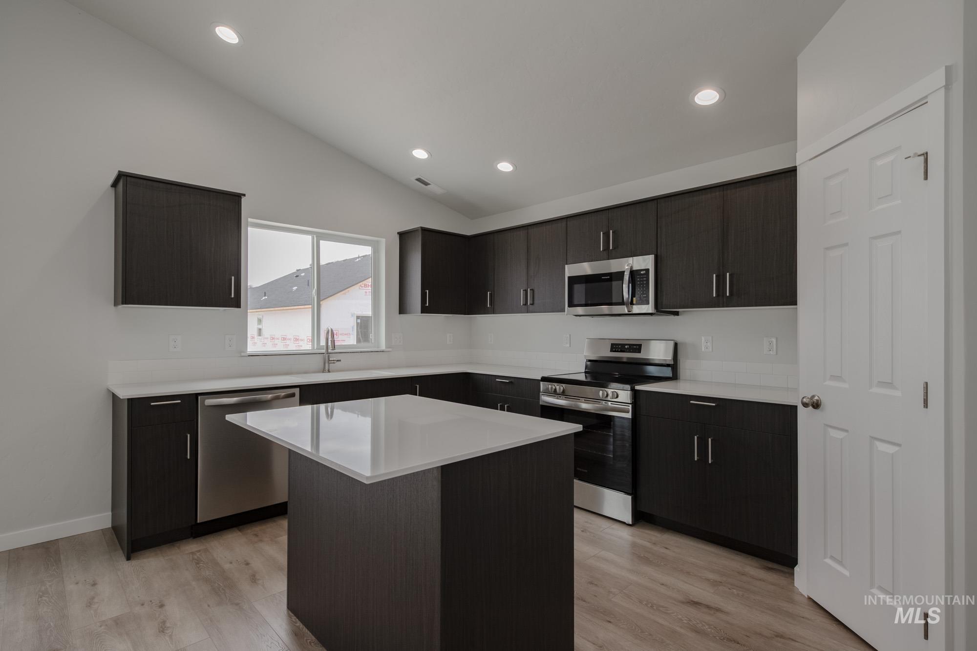Kitchen featuring stainless steel appliances, lofted ceiling, light wood-style floors, a kitchen island, and recessed lighting