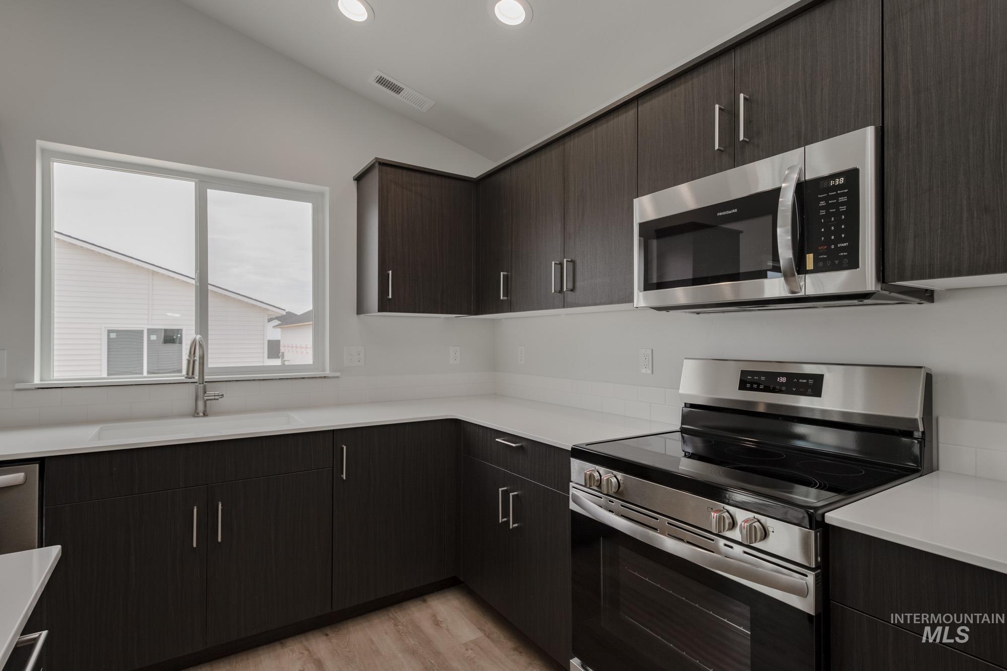 Kitchen with stainless steel appliances, modern cabinets, light wood finished floors, dark brown cabinetry, and recessed lighting