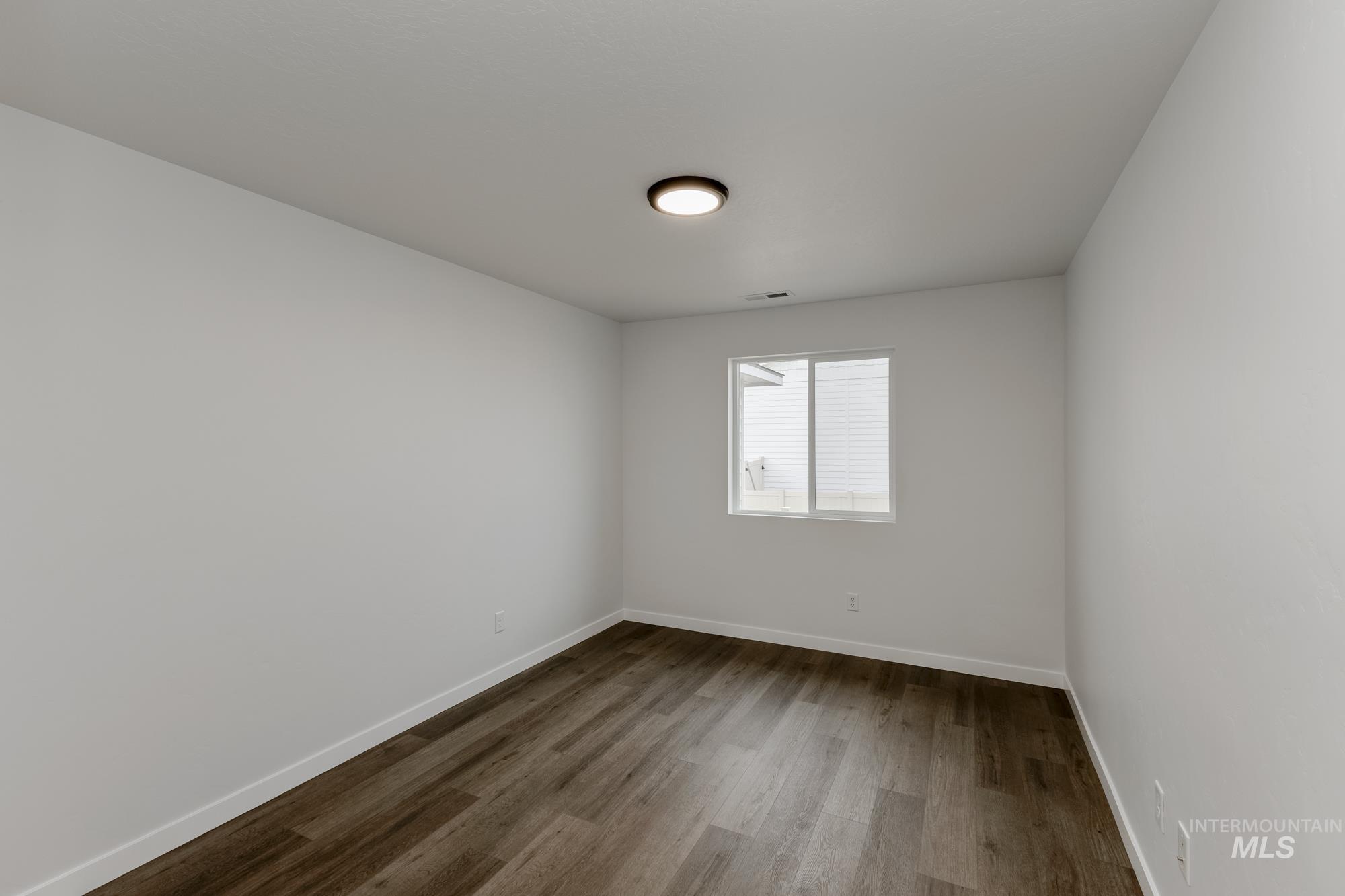 Spare room featuring dark wood-type flooring and baseboards
