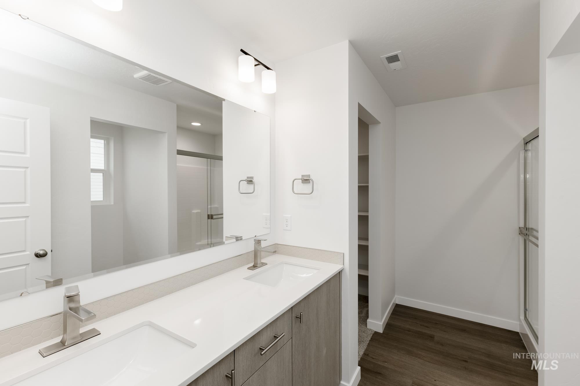 Bathroom with a stall shower, double vanity, a walk in closet, and dark wood finished floors