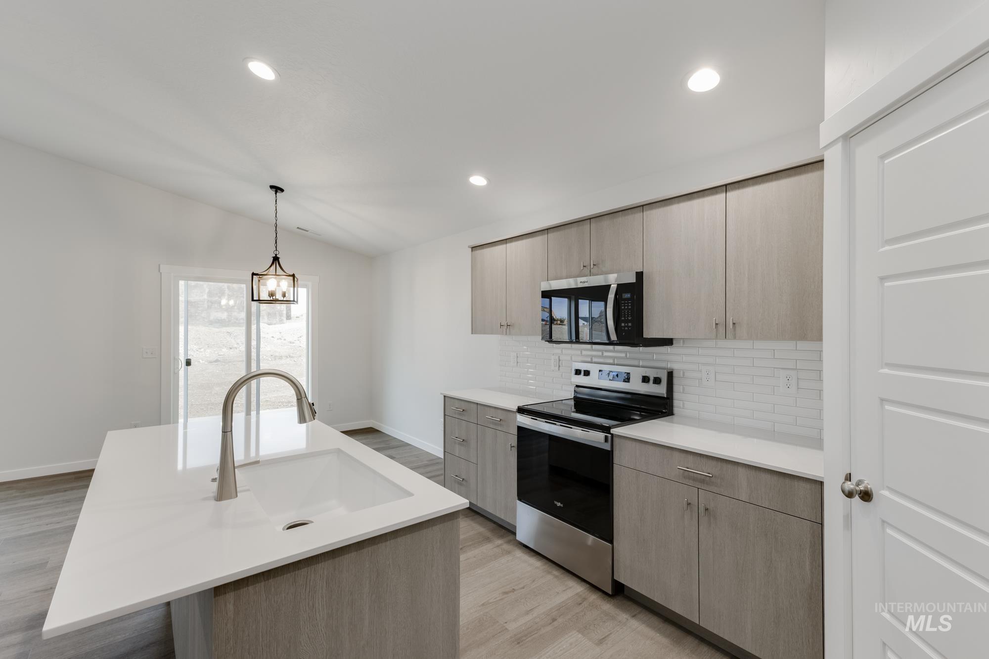 Kitchen with appliances with stainless steel finishes, tasteful backsplash, light brown cabinetry, pendant lighting, and lofted ceiling