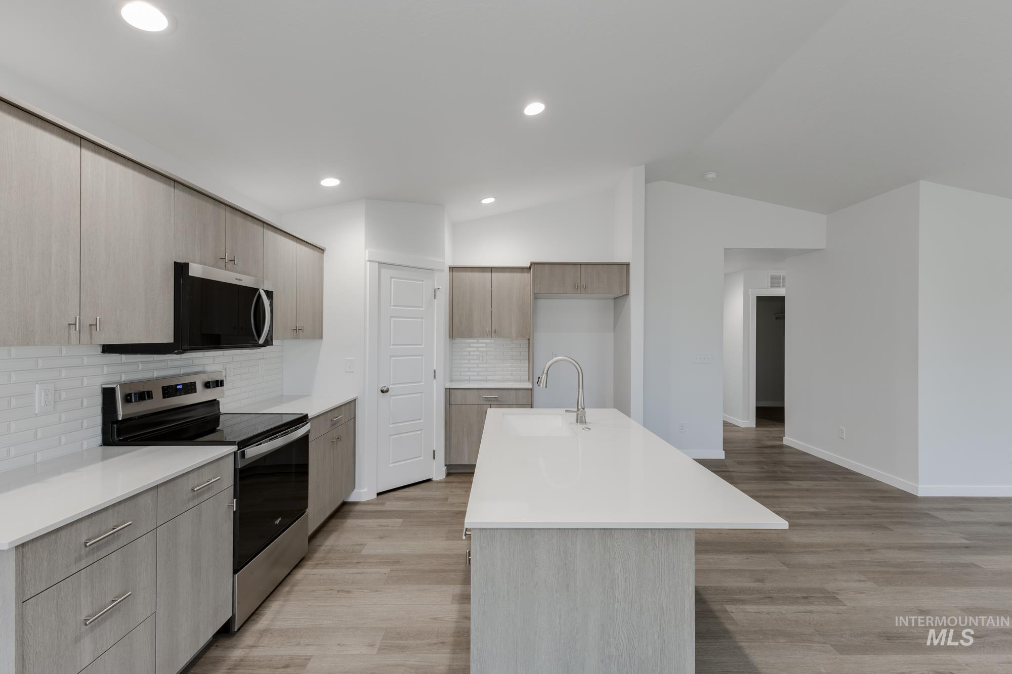 Kitchen featuring stainless steel appliances, tasteful backsplash, modern cabinets, lofted ceiling, and light wood-style flooring