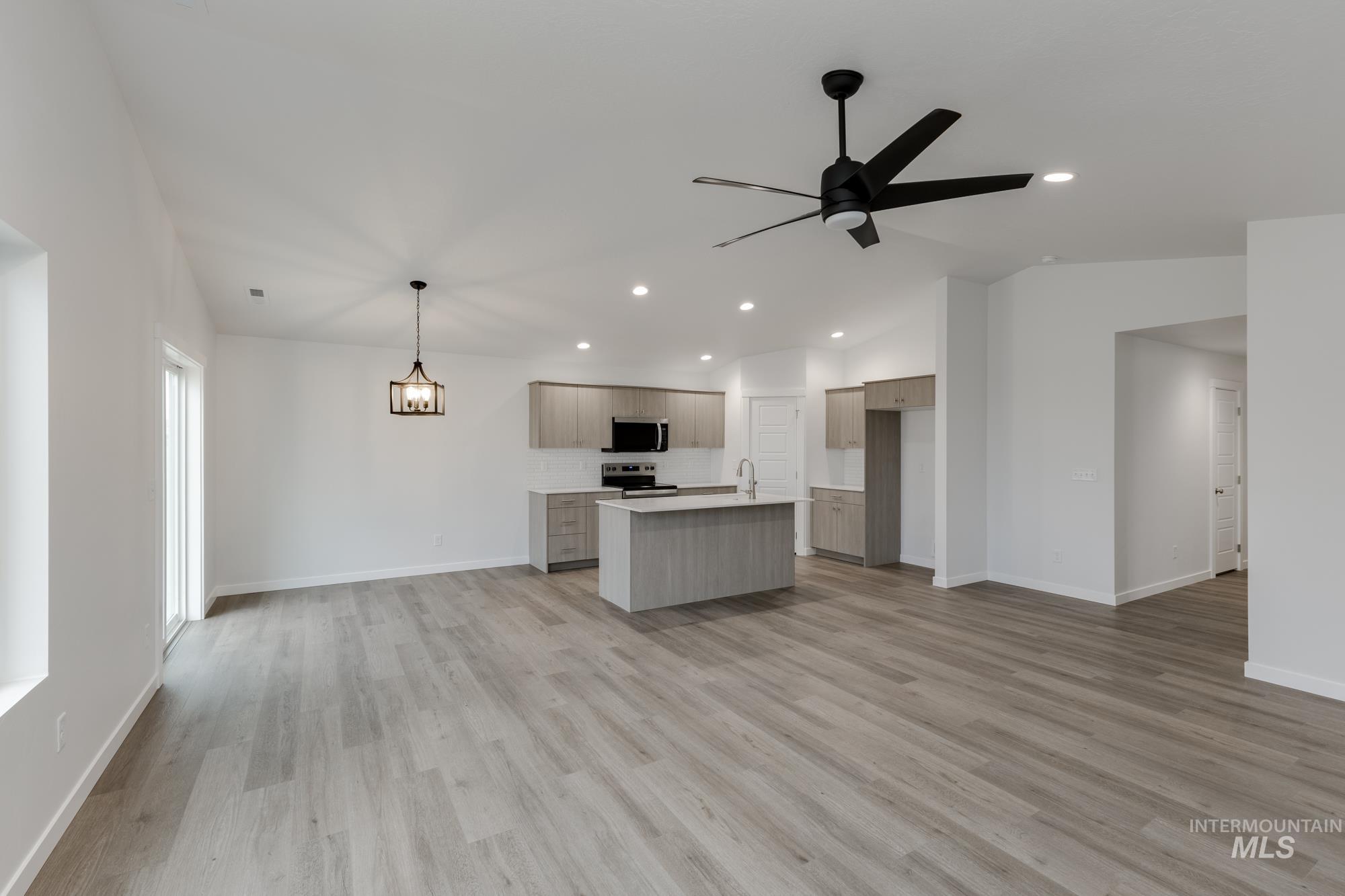 Kitchen with open floor plan, light countertops, a kitchen island with sink, lofted ceiling, and light wood-type flooring