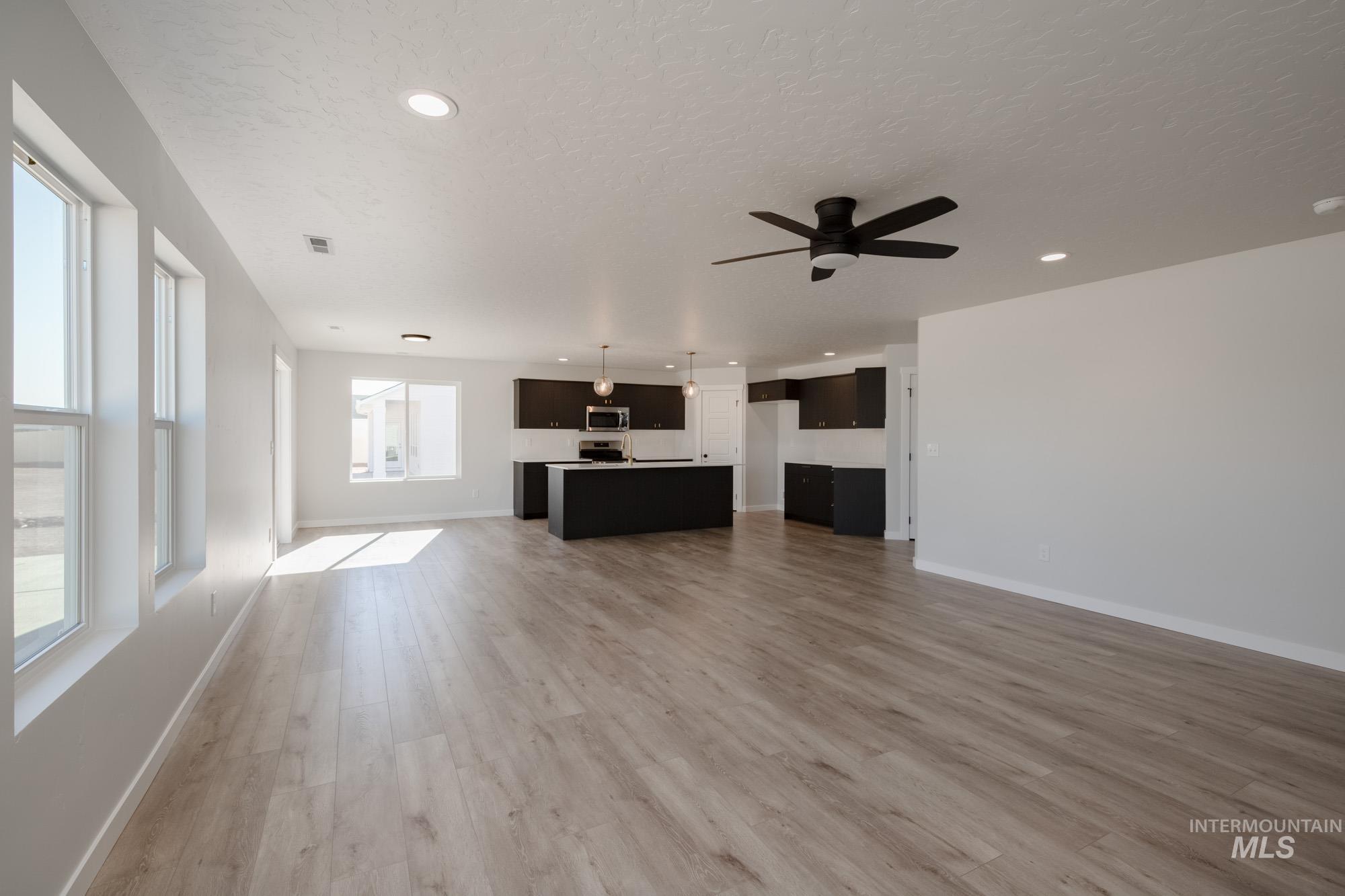 Unfurnished living room featuring light wood-type flooring, a textured ceiling, a ceiling fan, and recessed lighting